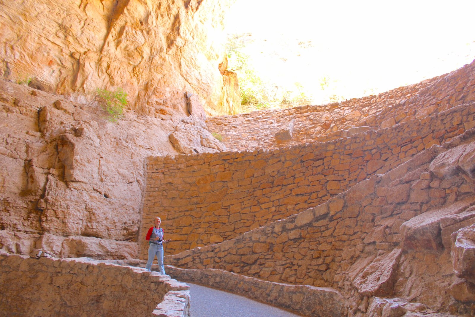 Woman in denim overalls hiking down the winding stone switchback path into the Natural Entrance of Carlsbad Caverns.
