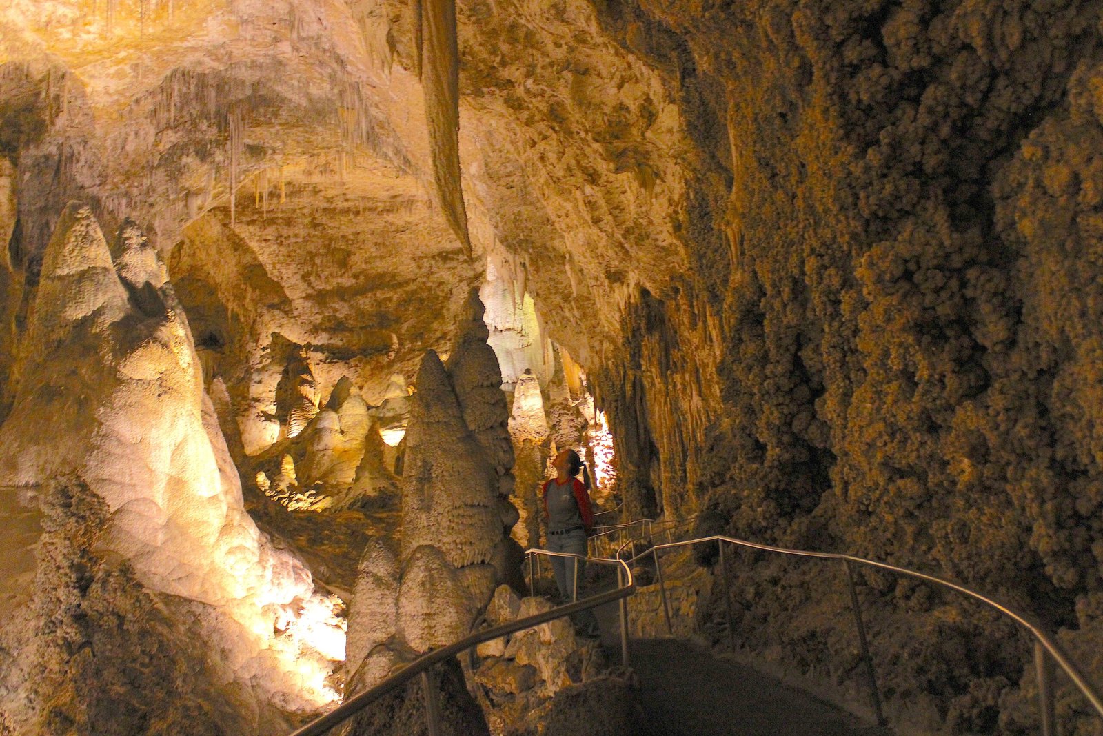 Woman standing on a cave trail gazing up at towering stalactites and complex rock formations inside Carlsbad Caverns.