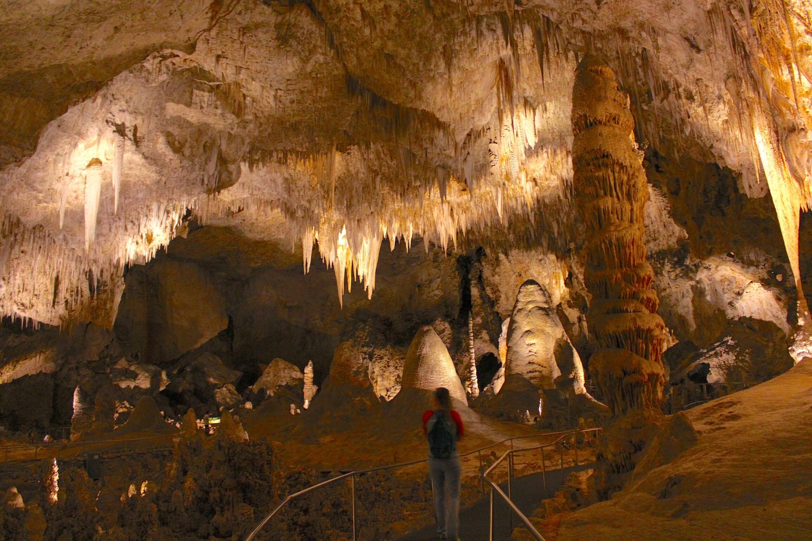 Woman walking along the illuminated paved pathway of the massive Big Room underground chamber at Carlsbad Caverns.