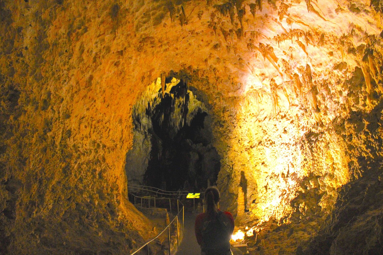 Woman walking along a winding paved cavern path toward a natural rock arch inside Carlsbad Caverns.