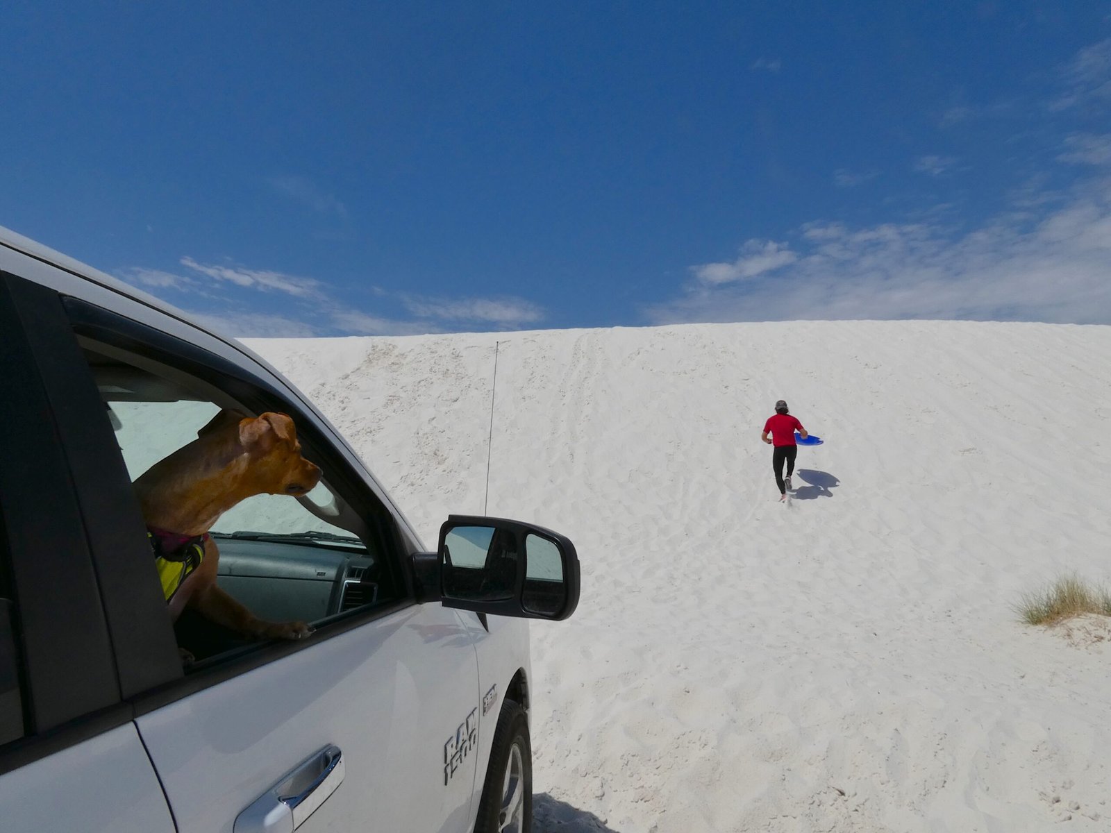 A man trekking up a steep slope of bright white gypsum sand at White Sands National Park in New Mexico.