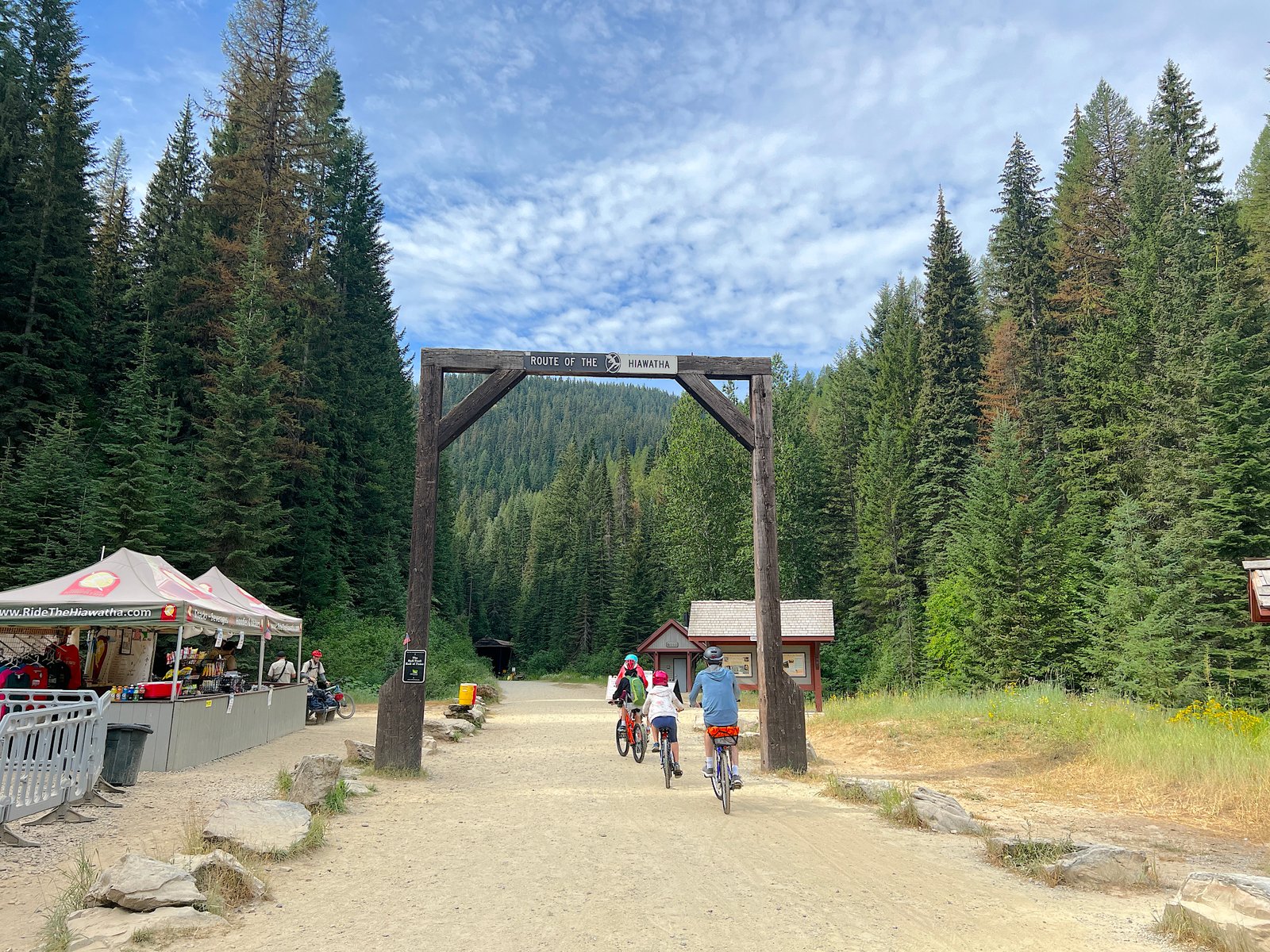 Bicyclists riding under the official wooden Route of the Hiawatha trailhead sign at the start of the trail.