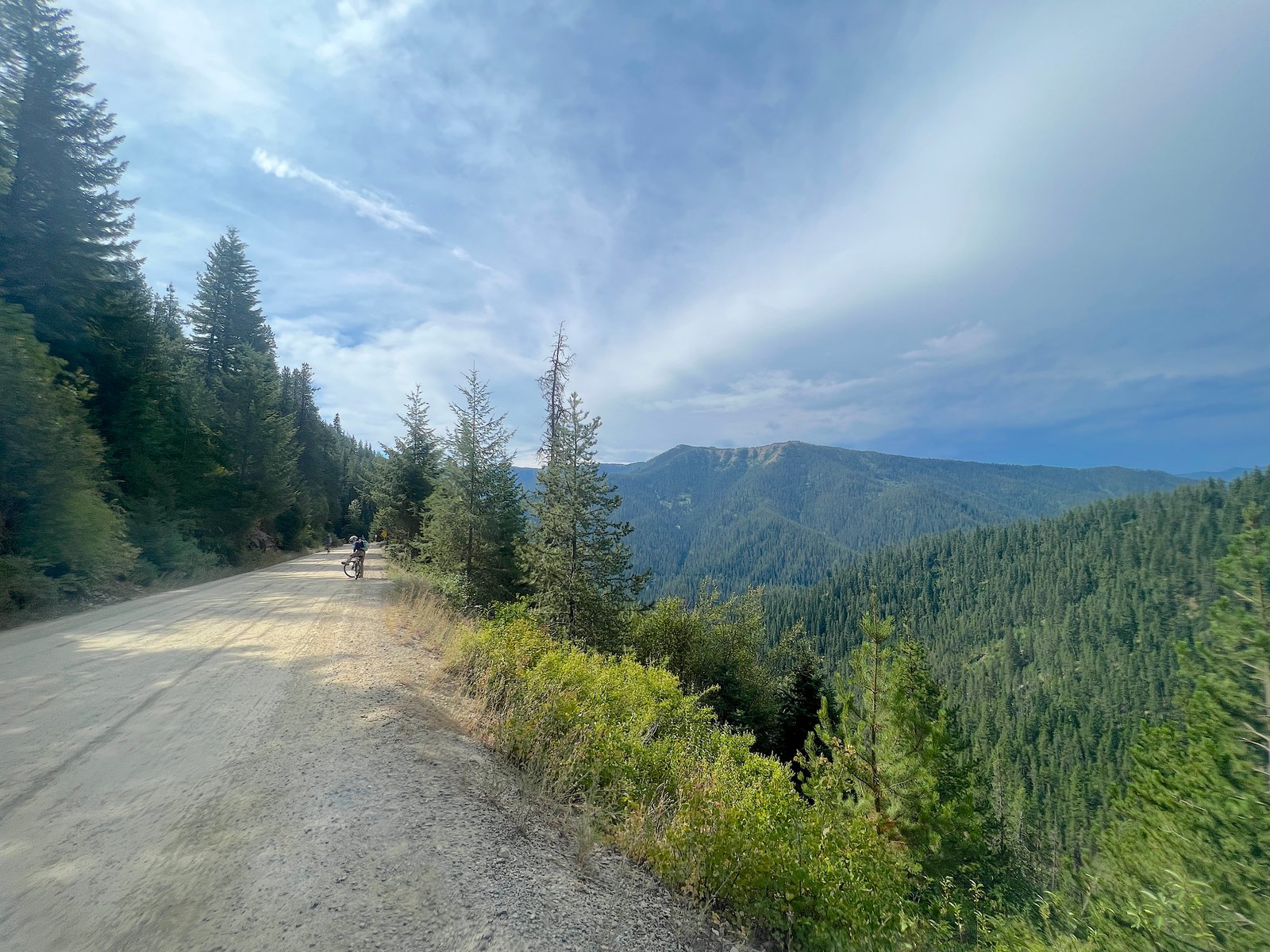 Cyclist riding a bicycle on a wide gravel dirt path featuring expansive, open mountain views of the Bitterroots on the Route of the Hiawatha.