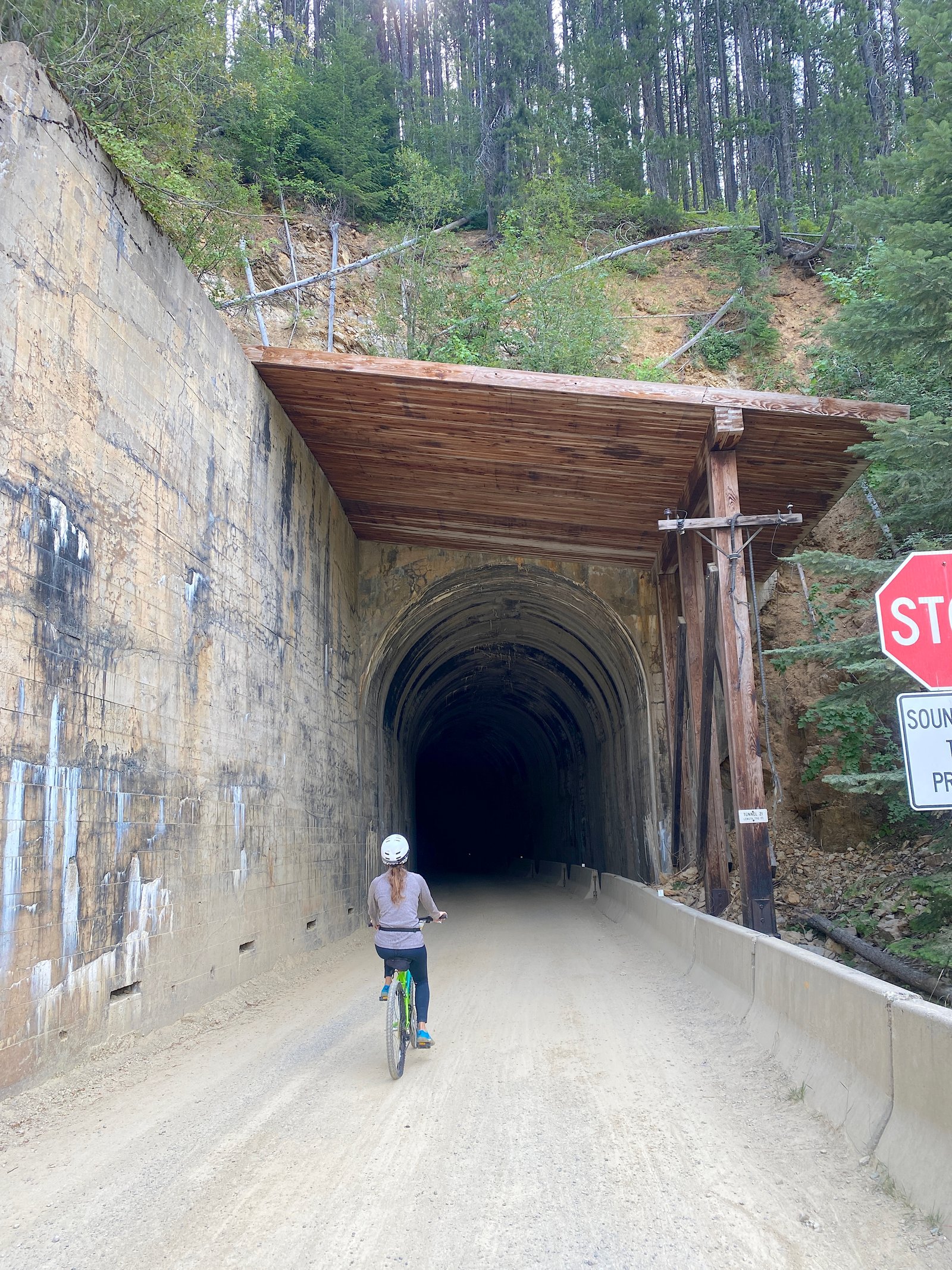 Close-up shot of a female cyclist on a bike riding along a gravel trail toward the pitch-black entrance of a mountain tunnel on the Route of the Hiawatha.