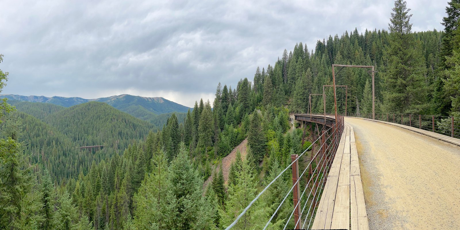 Panoramic landscape view of a historic wooden railroad trestle bridge spanning a deep forest canyon in the Bitterroot Mountains on the Route of the Hiawatha.