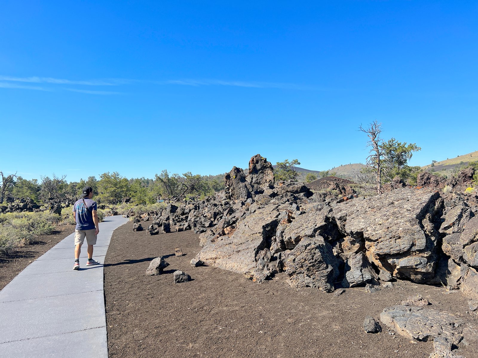 Hiker walking along the paved Devil's Orchard trail next to massive black basalt lava rocks at Craters of the Moon