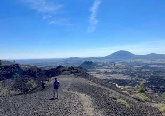Hiker standing on a scenic trail overlooking the volcanic cinder cones and lava fields at Craters of the Moon National Monument