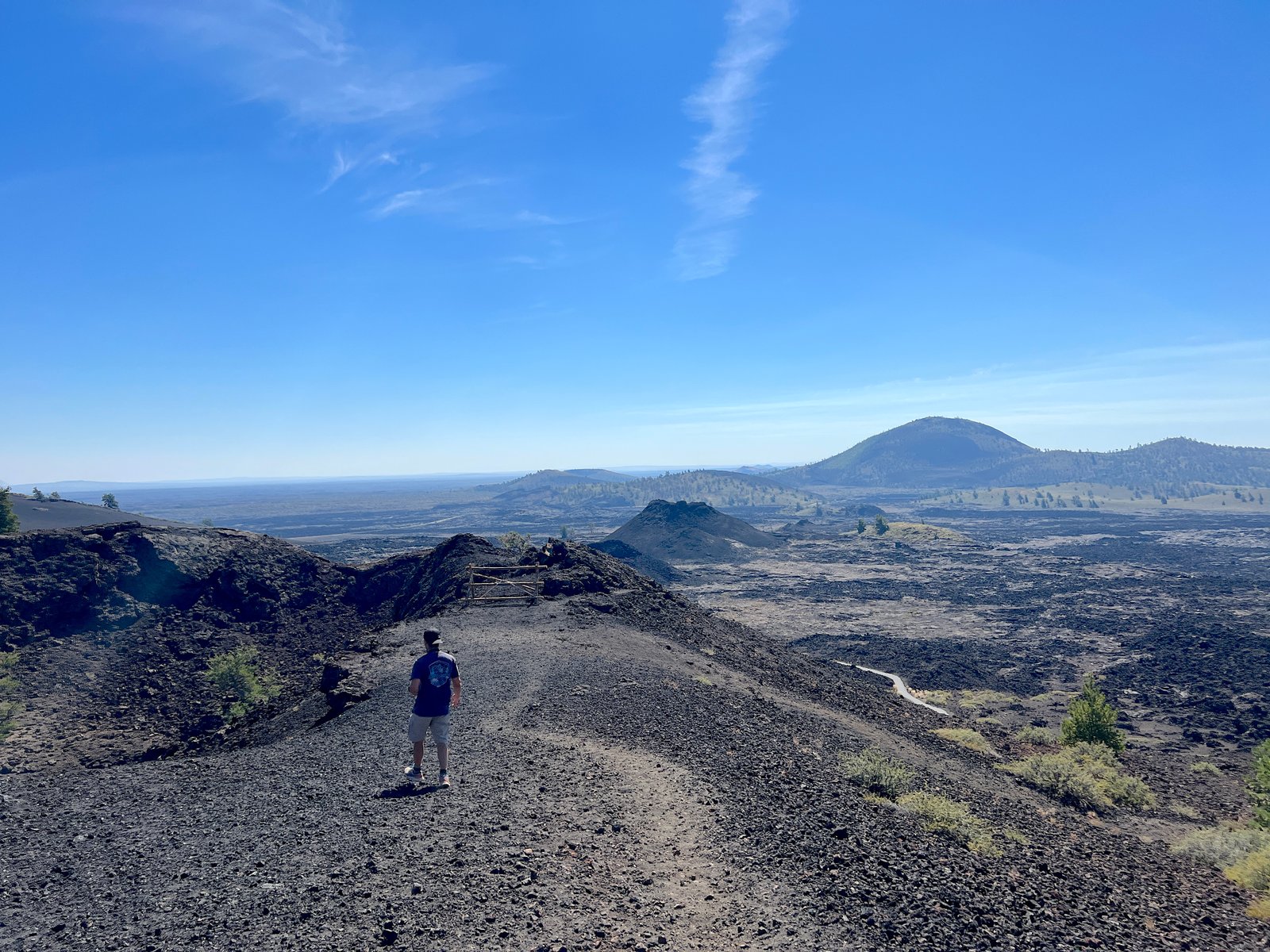 Hiker standing on a scenic trail overlooking the volcanic cinder cones and lava fields at Craters of the Moon National Monument