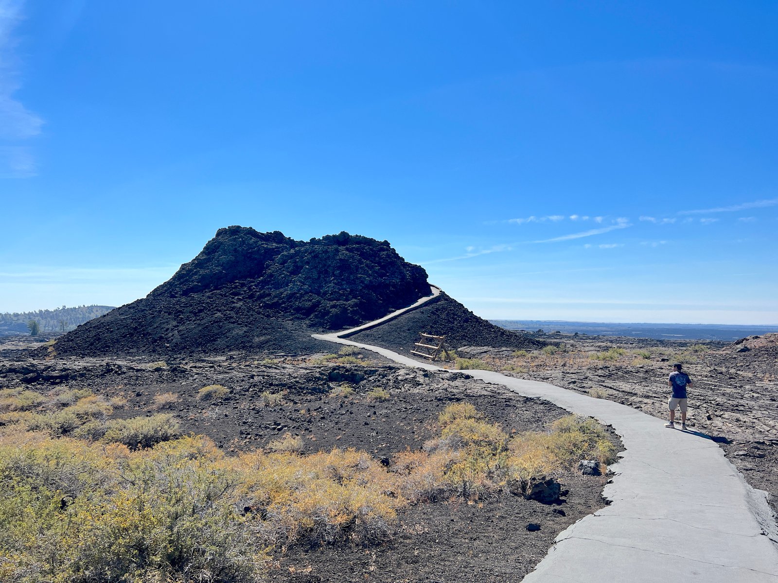 Hiker walking along the paved trail leading to a large volcanic spatter cone at Craters of the Moon