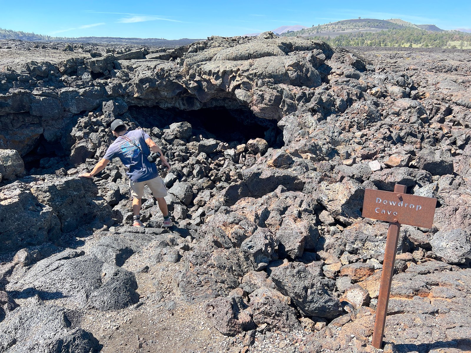 Hiker carefully climbing down steep lava rocks into the entrance of Dewdrop Cave at Craters of the Moon