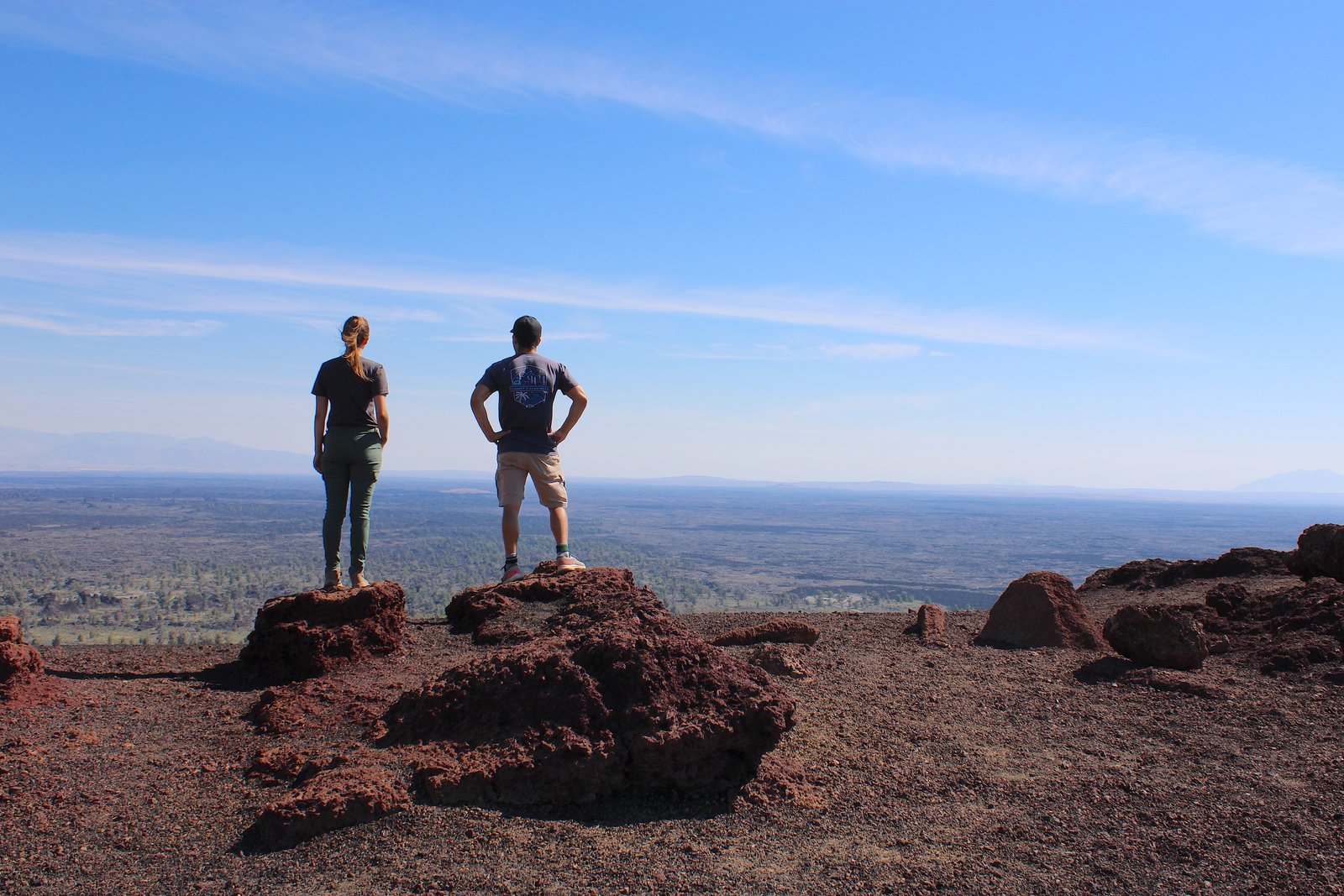 Two hikers standing on volcanic lava rock at the summit of Inferno Cone looking over Craters of the Moon National Monument