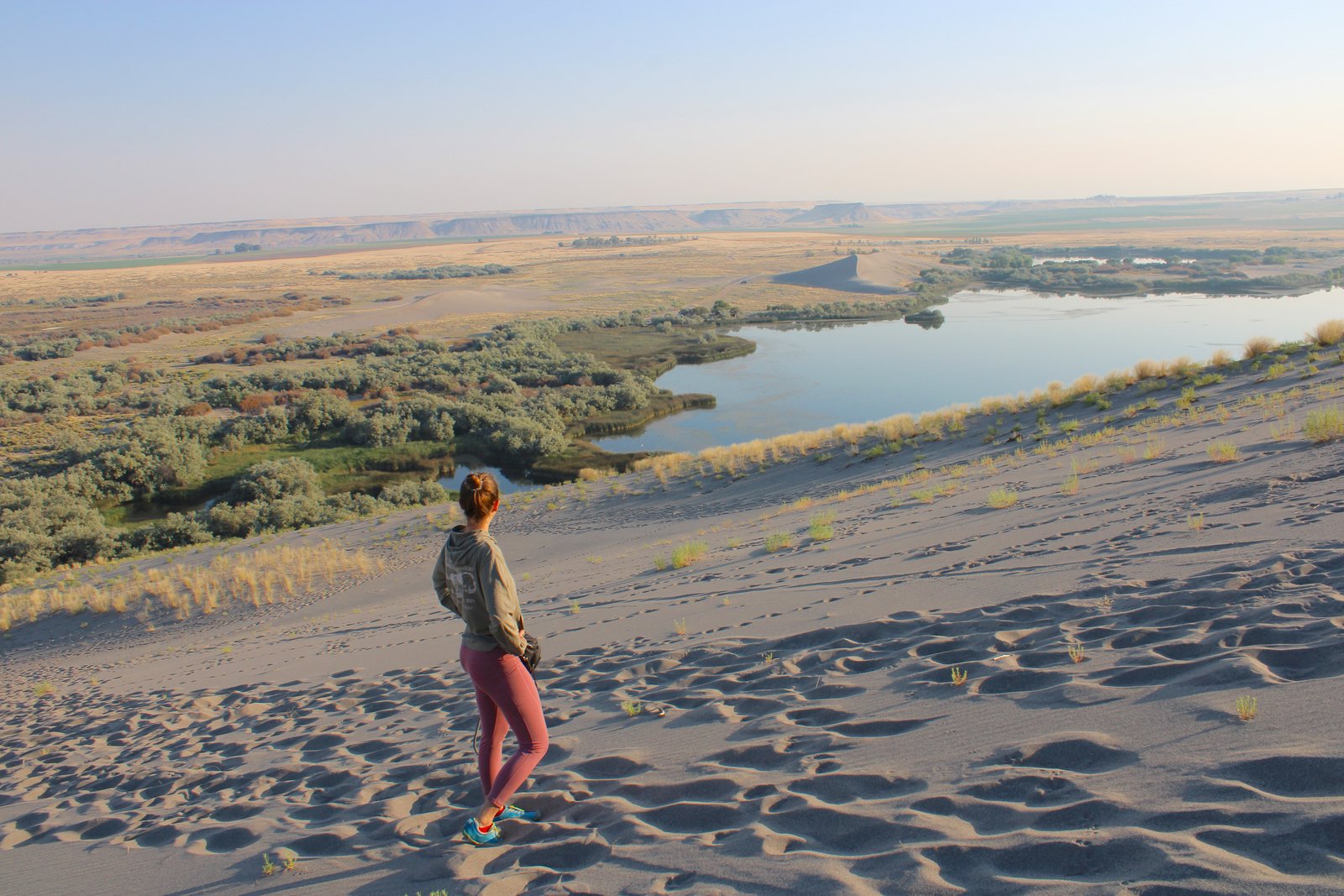 A visitor looking out at the desert lake surrounded by sand dunes at Bruneau Dunes State Park in Idaho.