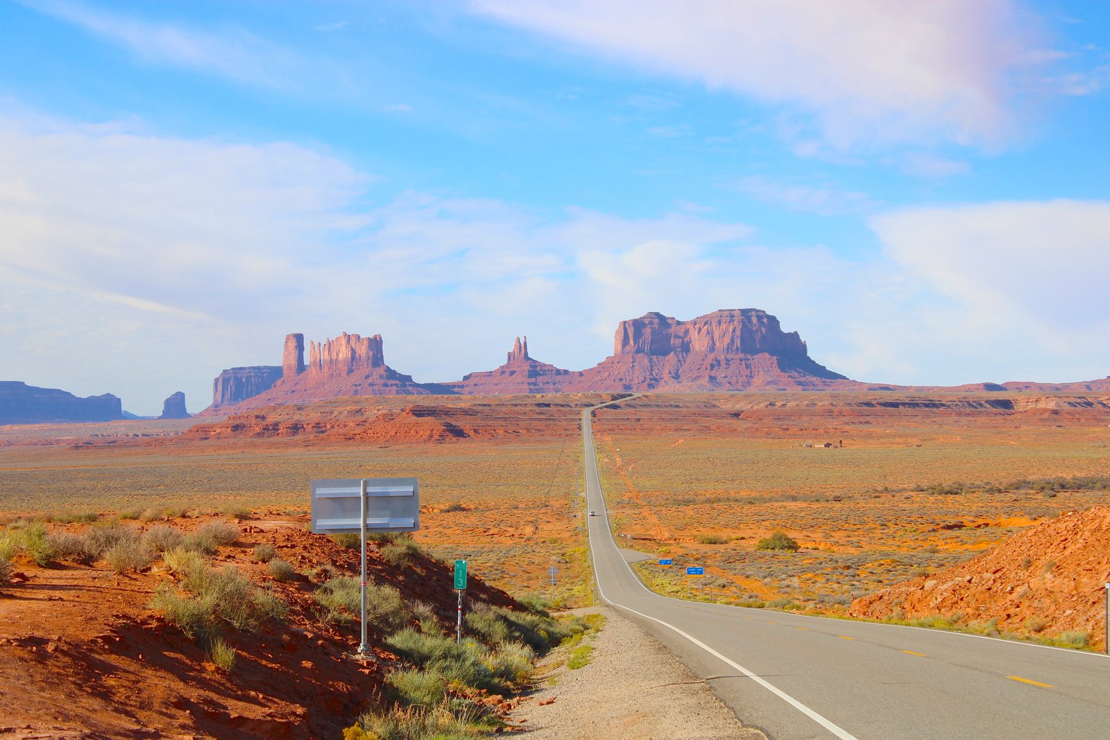 road with red rocks in the distance below blue sky and clouds