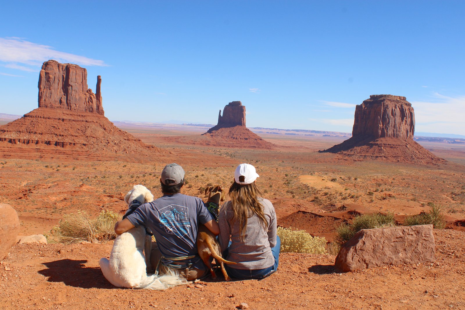 two people and two dogs sitting looking out at red rocks in the distance