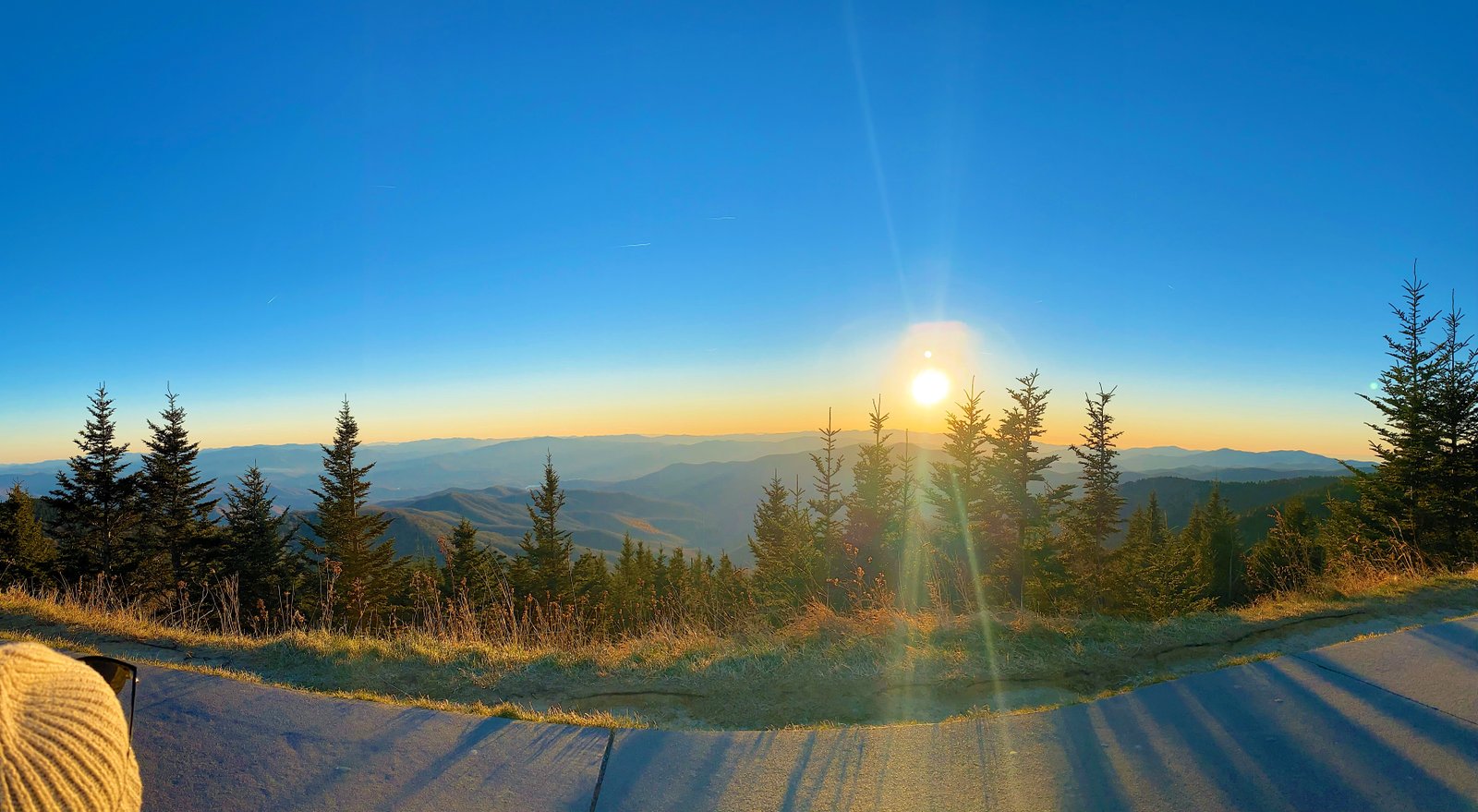 A breathtaking sunset casting a warm golden and orange glow over endless blue mountain ridges from the open overlook at the Clingmans Dome parking lot in the Great Smoky Mountains National Park.