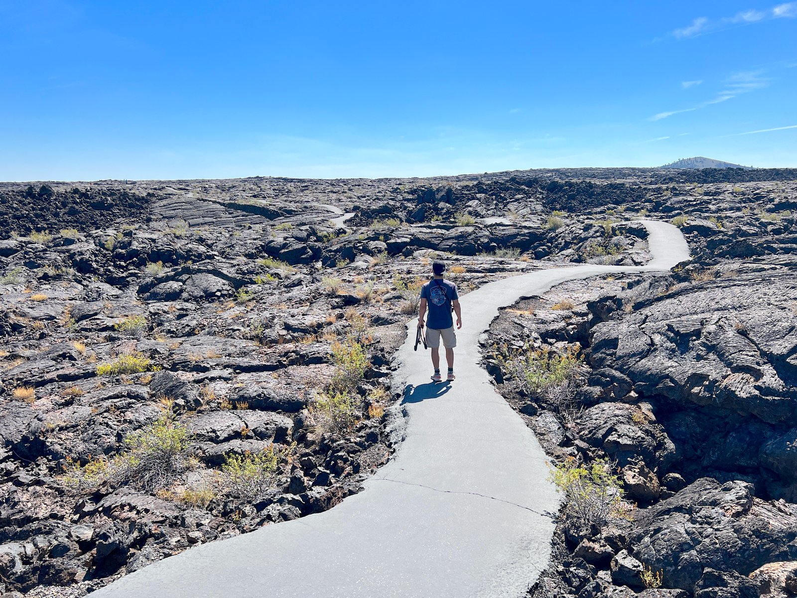 Hiker walking along a paved trail surrounded by black basalt lava fields at Craters of the Moon National Monument in Idaho