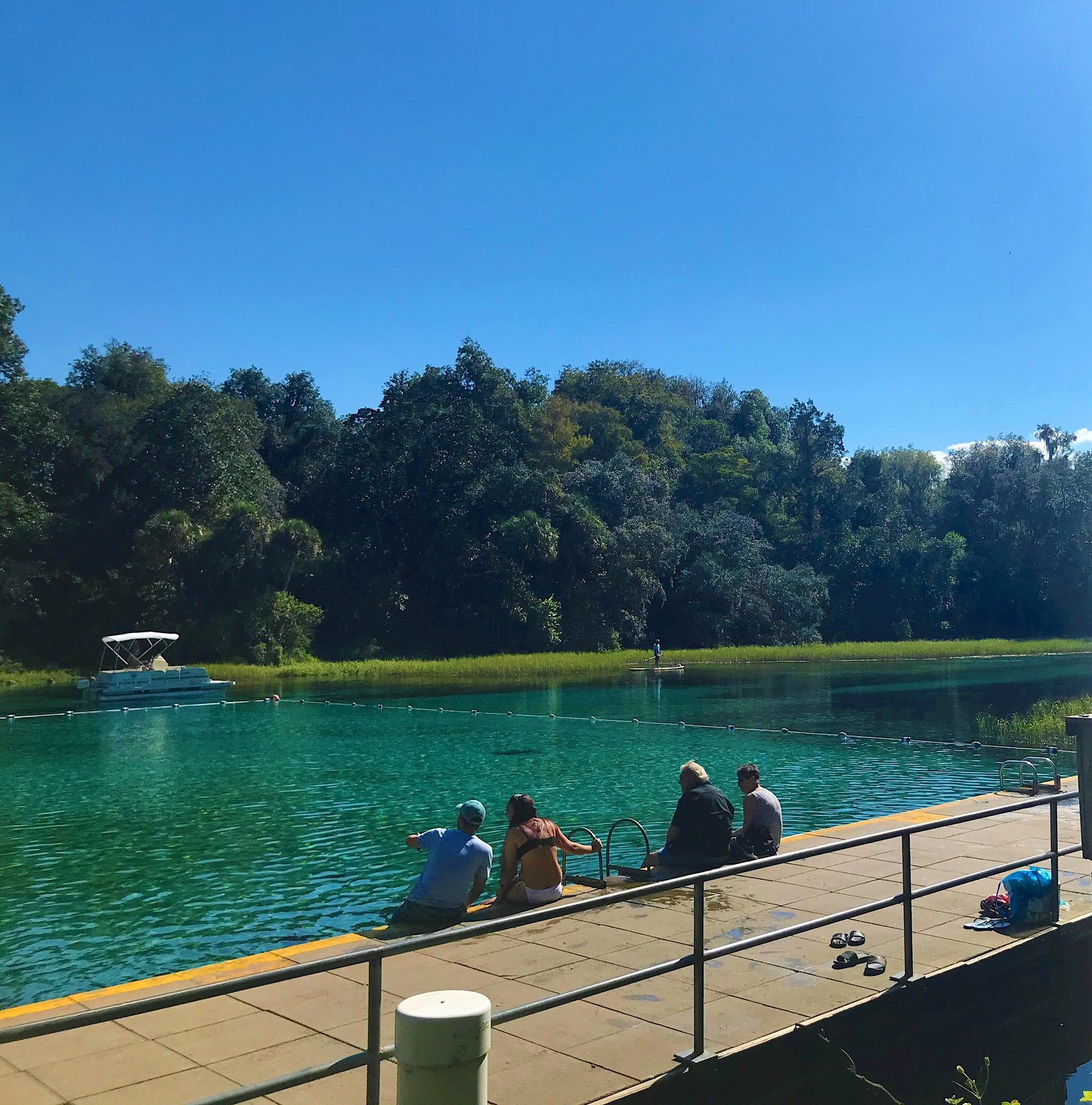 People sitting on the elevated wooden platform entrance and jumping-off point overlooking the crystal-clear spring water at Rainbow Springs State Park.