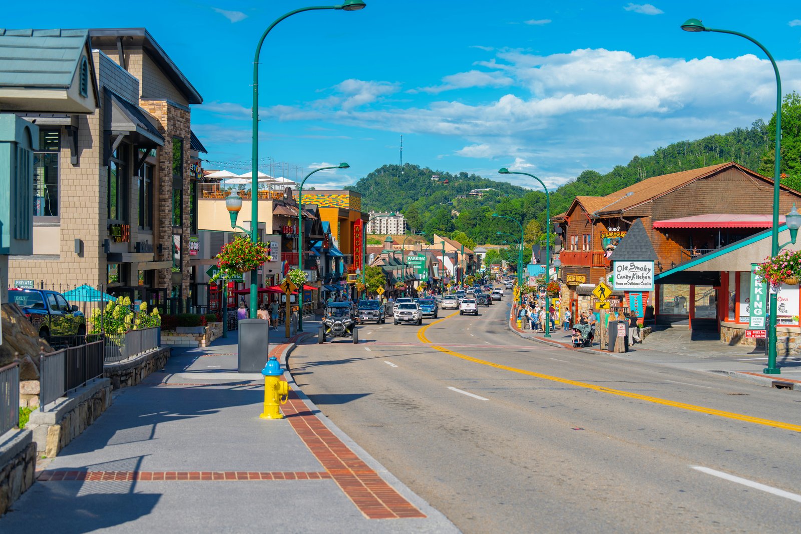 The vibrant downtown street of Gatlinburg filled with shops, restaurants, and mountain architecture with forested peaks rising in the background.
