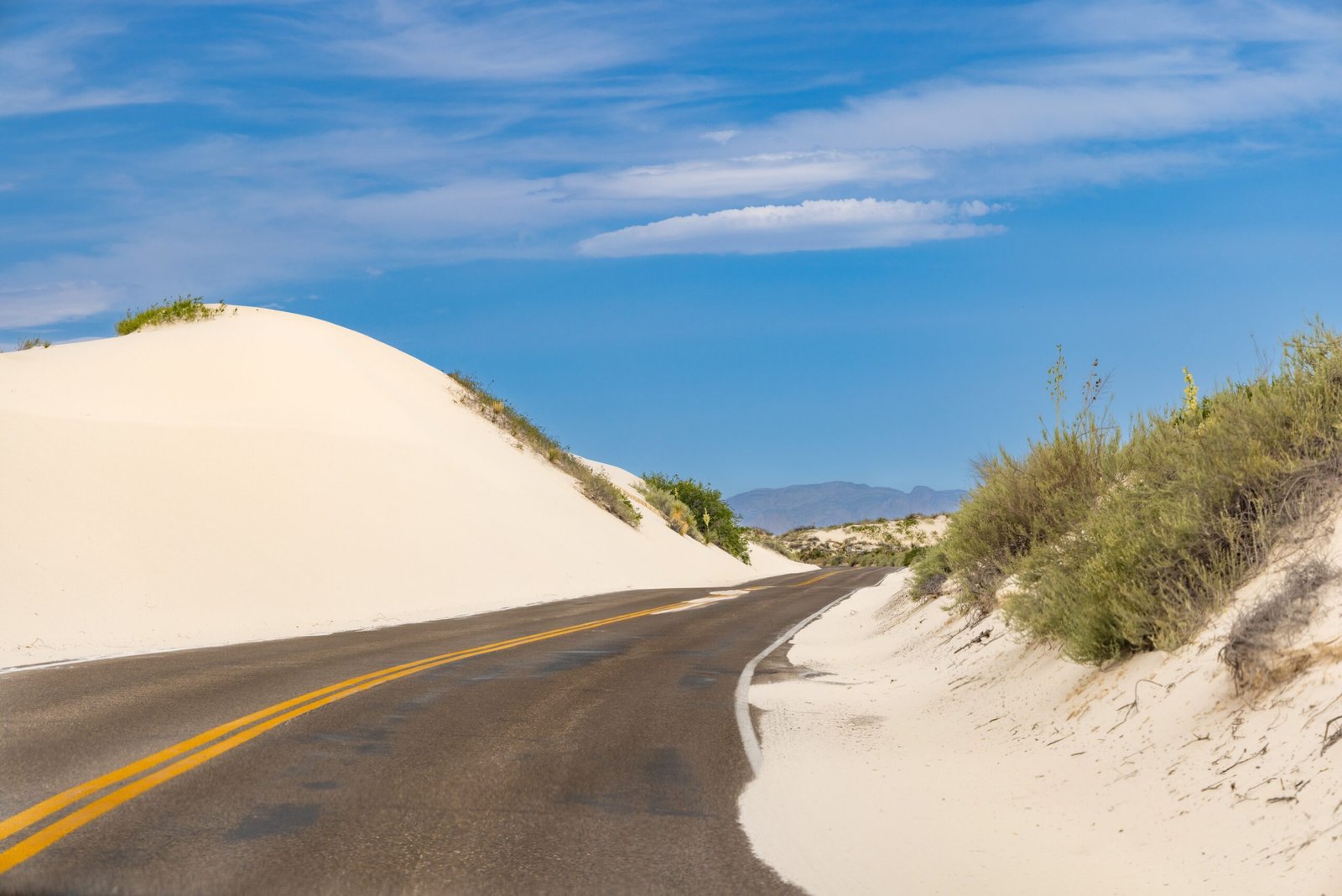 The paved Dunes Drive winding between towering white gypsum sand dunes under a clear blue sky at White Sands National Park.