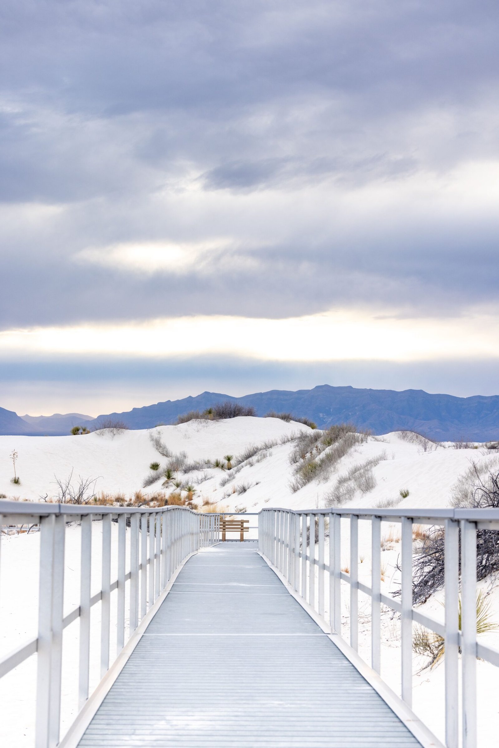 An elevated wooden boardwalk winding through the white gypsum dunes at White Sands National Park in New Mexico.