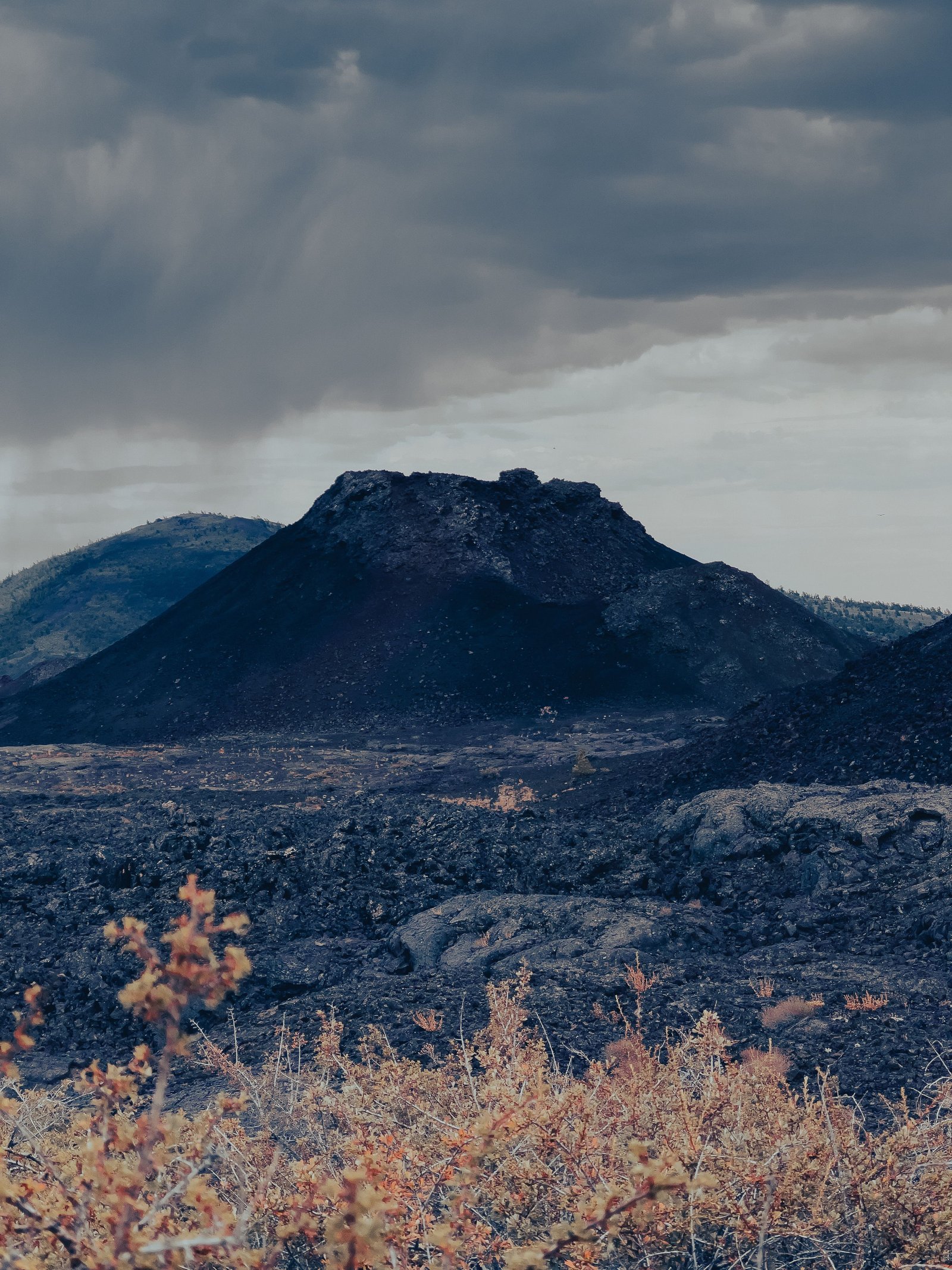 Volcanic cinder cone and lava field under dramatic cloudy sky at Craters of the Moon National Monument in Idaho