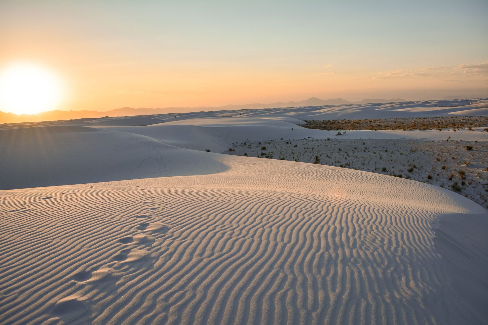 Warm golden hour sun glow lighting up the horizon and rolling white gypsum dunes at sunset in White Sands National Park, New Mexico.