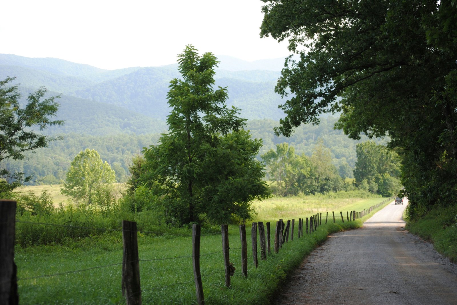 A gravel pathway running alongside a wooden fence and green fields with distant mountains in the Cades Cove valley of the Great Smoky Mountains National Park.