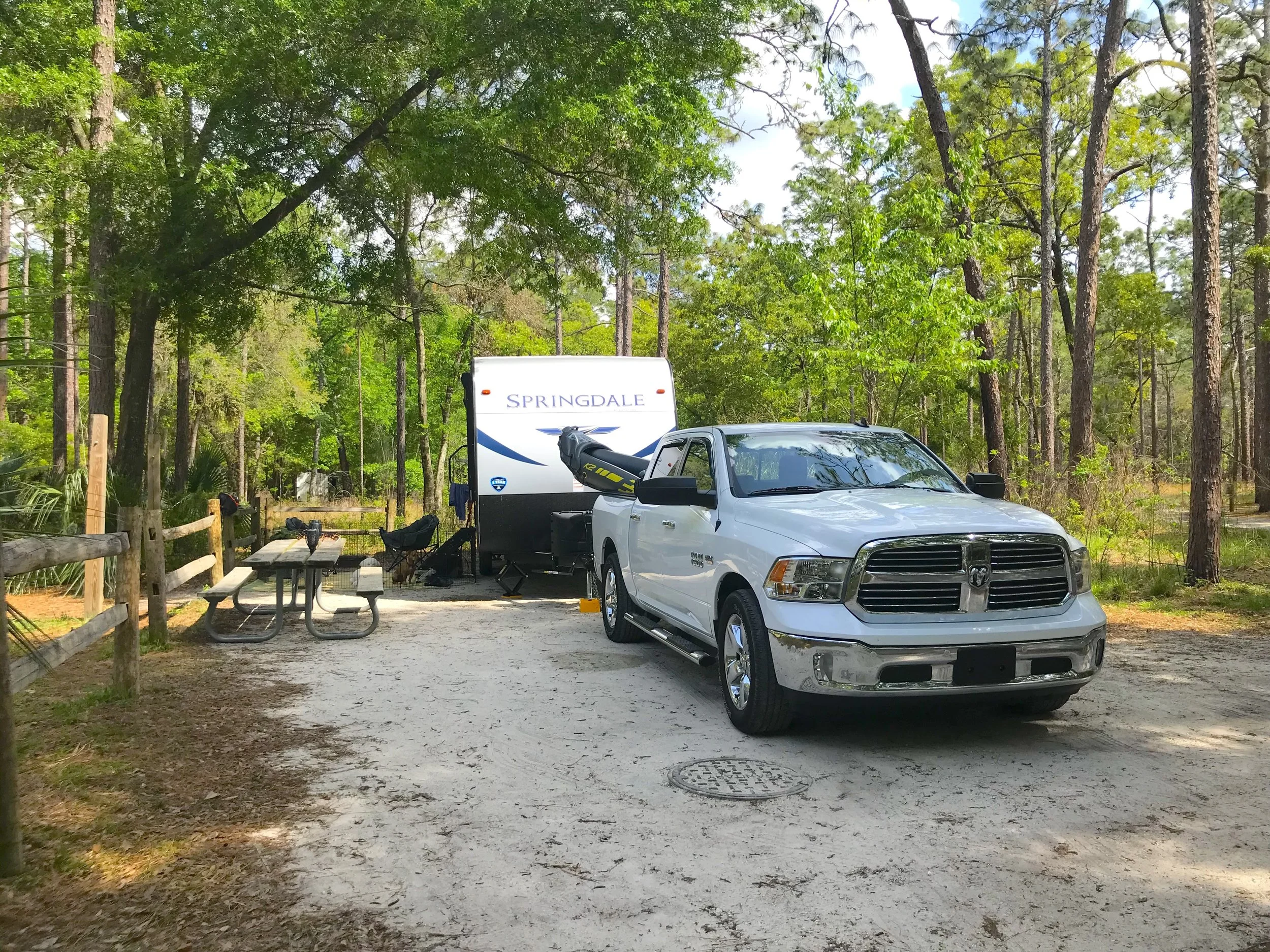 A travel trailer and truck parked in a shaded wooded campsite at the Wekiwa Springs State Park campground.