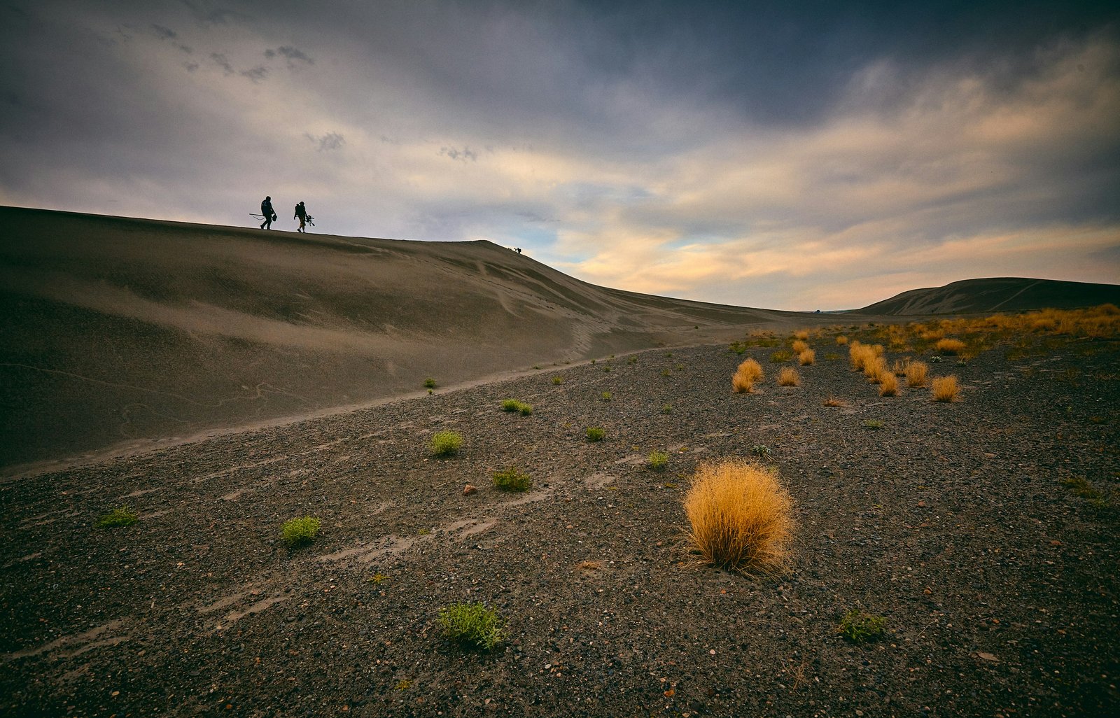 Two hikers walking along the crest of a massive sand dune at Bruneau Dunes State Park in Idaho.