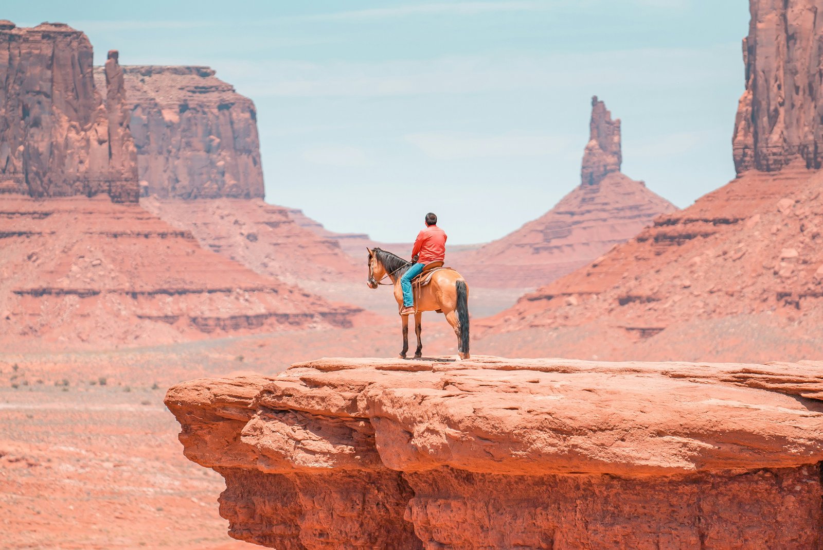 man sitting on horse with red rocks in the distance