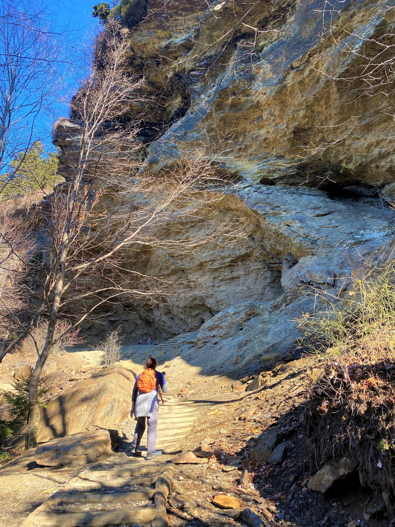 Hikers walking along the mountain trail approaching the massive stone overhang of Alum Cave Bluffs in the Great Smoky Mountains.