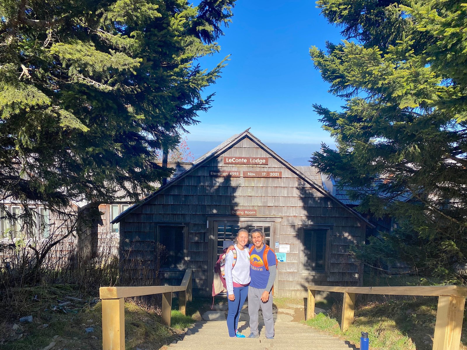A smiling couple standing in front of the historic wooden cabins at LeConte Lodge on Mount LeConte in Great Smoky Mountains National Park.