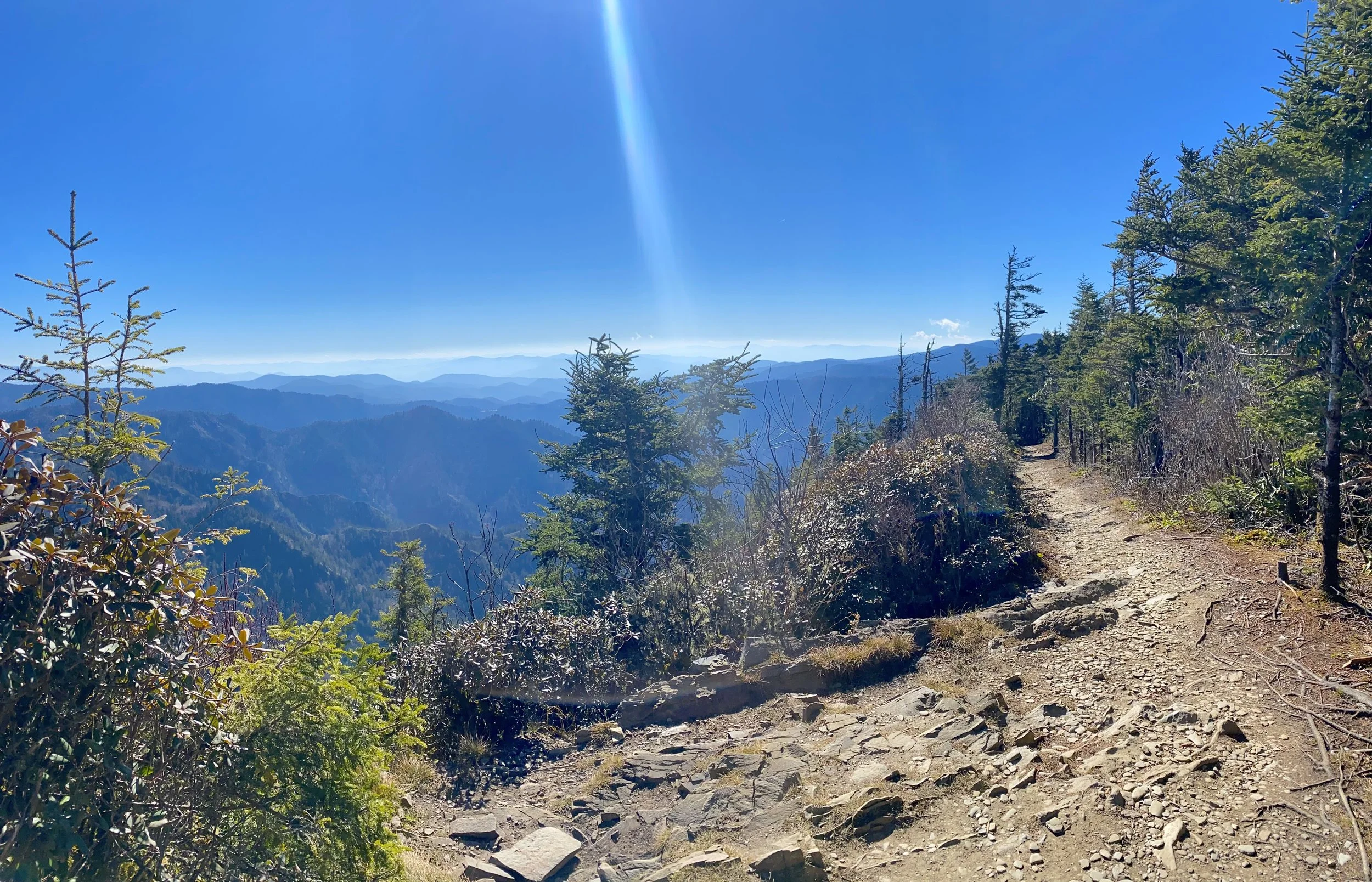 A scenic view of the trail hugging the mountainside with expansive mountain vistas near the summit of Mount LeConte in the Great Smoky Mountains.