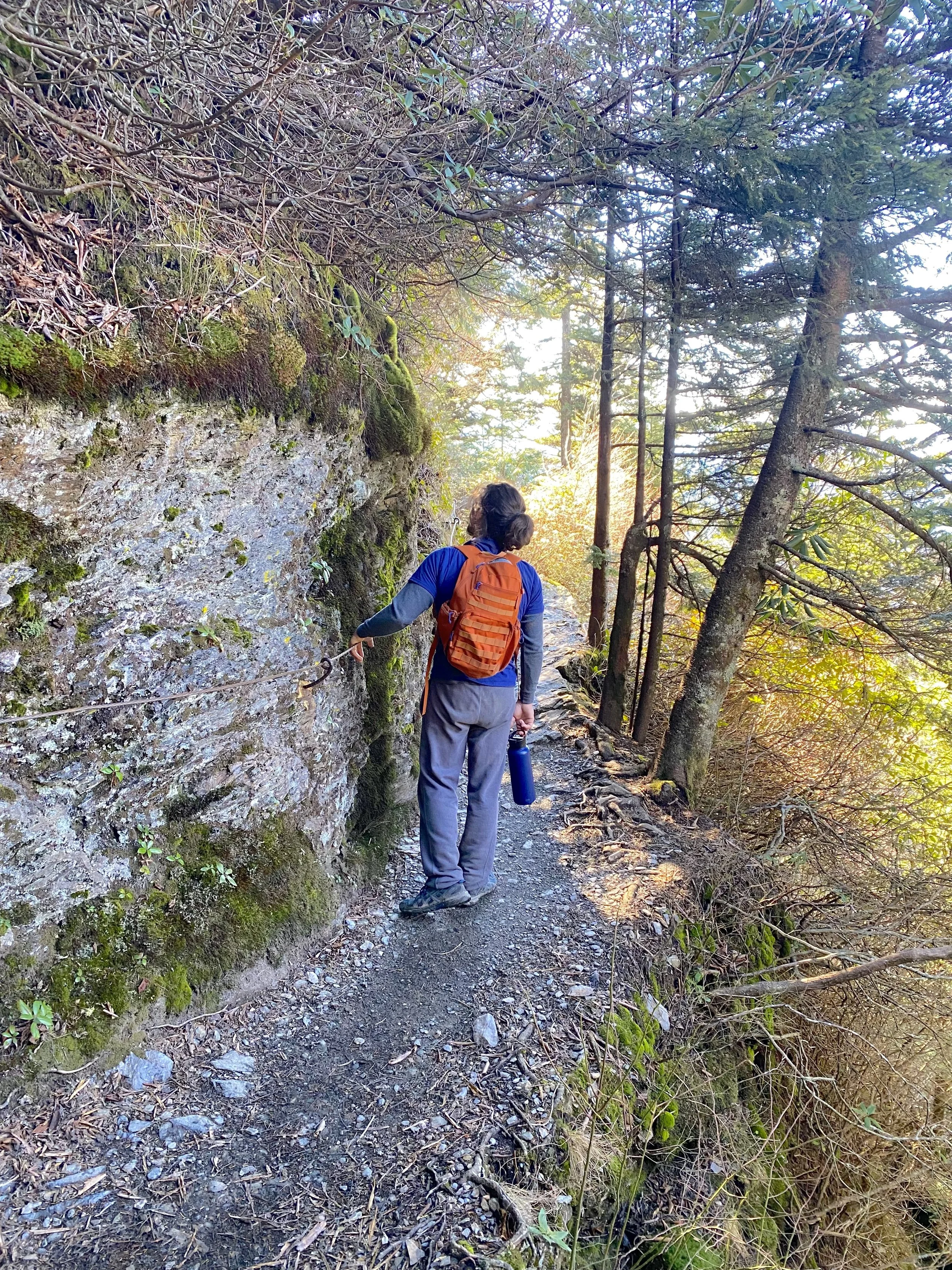 Hiker wearing a daypack with a water bottle on the cable-assisted section of the Alum Cave Trail in Great Smoky Mountains National Park.