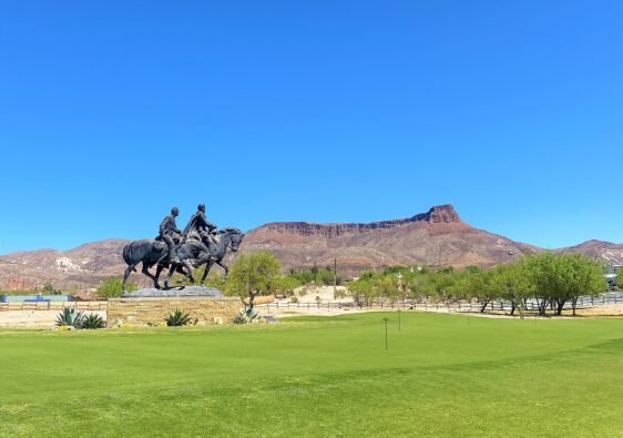 Lajitas Golf Resort manicured green grounds featuring a bronze cavalry statue with West Texas desert mountains in the background under a clear blue sky.