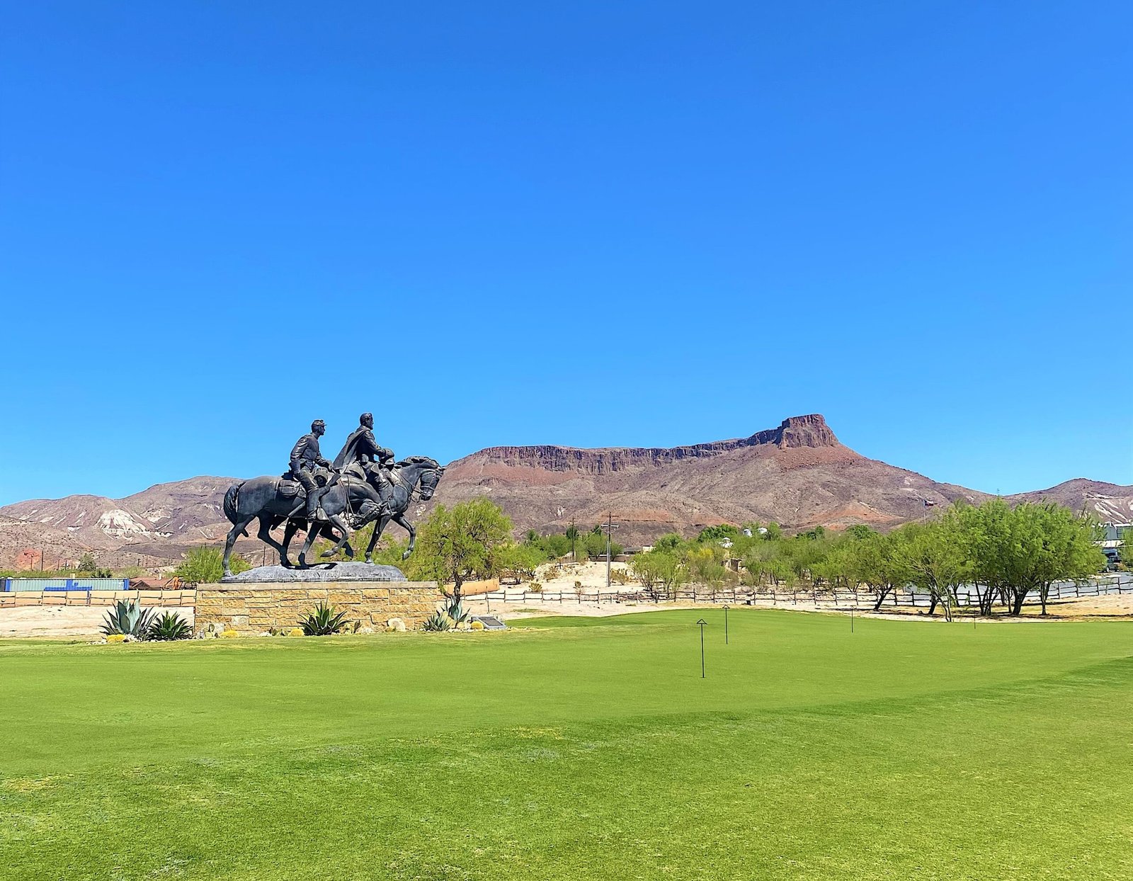 Lajitas Golf Resort manicured green grounds featuring a bronze cavalry statue with West Texas desert mountains in the background under a clear blue sky.