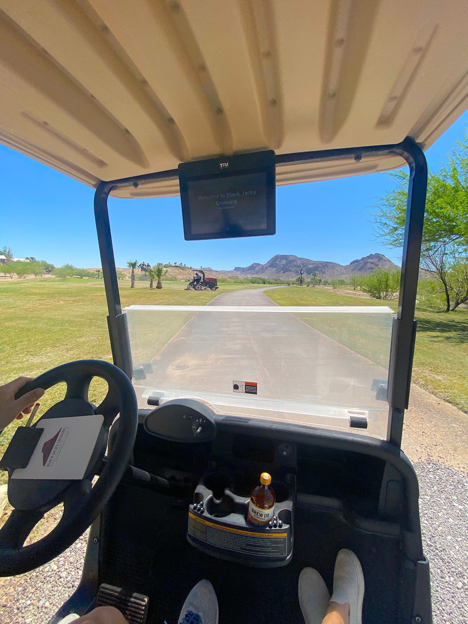 POV view from inside a golf cart driving along the manicured fairways and greens at Lajitas Golf Resort with desert mountains in the background.