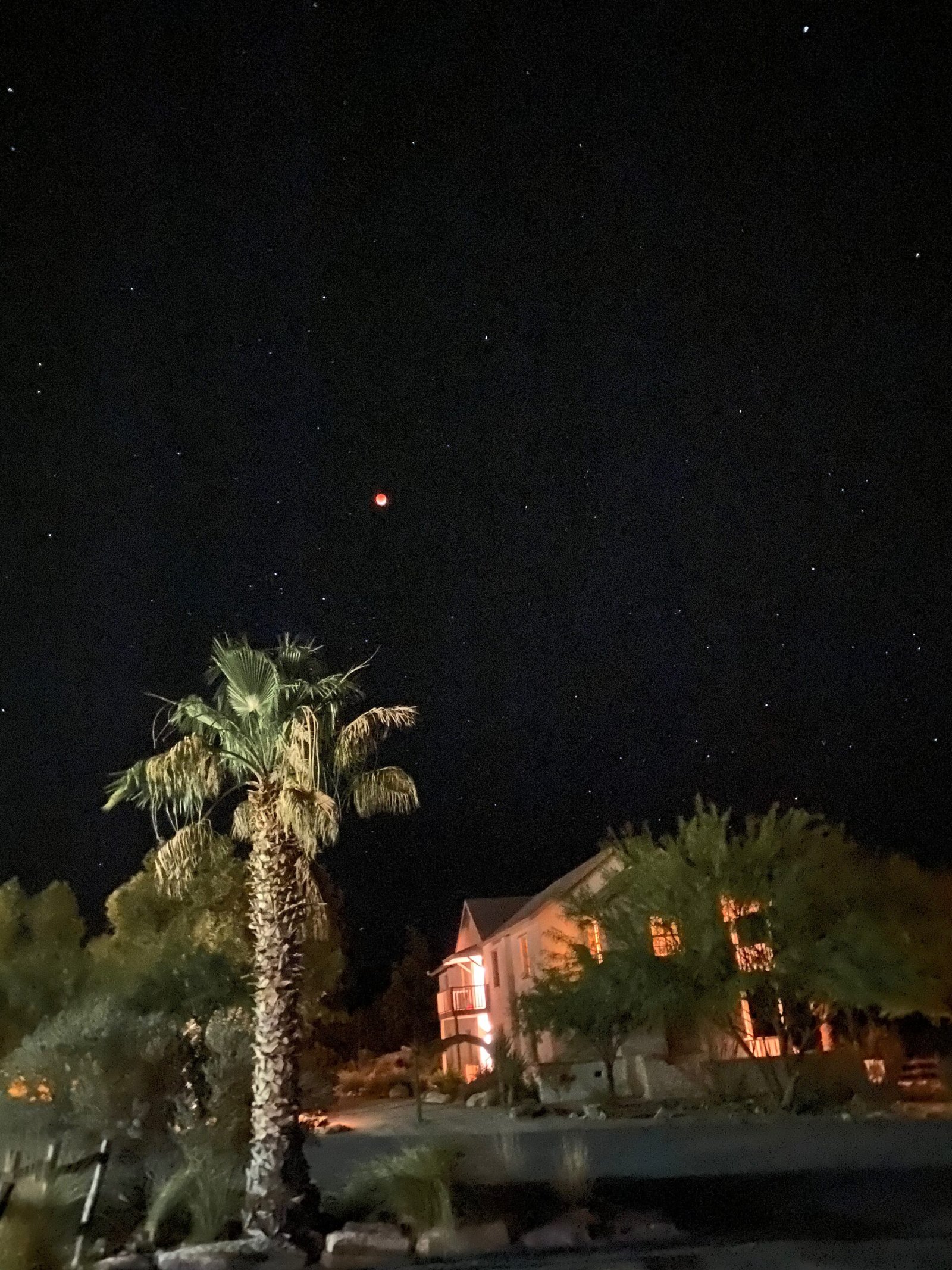 Deep red moon during a lunar eclipse shining in the dark night sky above resort buildings at Lajitas Golf Resort in West Texas.