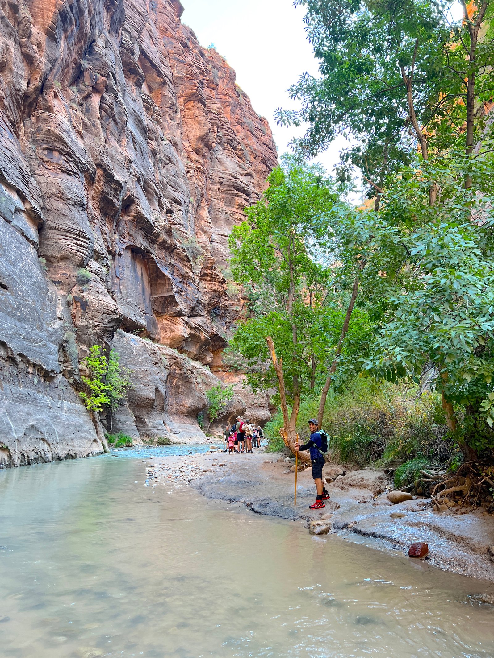 A hiker relaxing on a small sandy shoreline beside the flowing water inside The Narrows at Zion National Park.