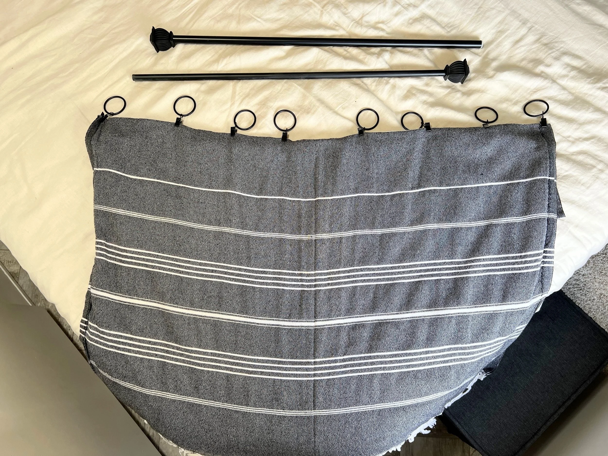 A curtain rod split apart with metal clips attached, laid out and ready to be hung on the wall over an RV window.