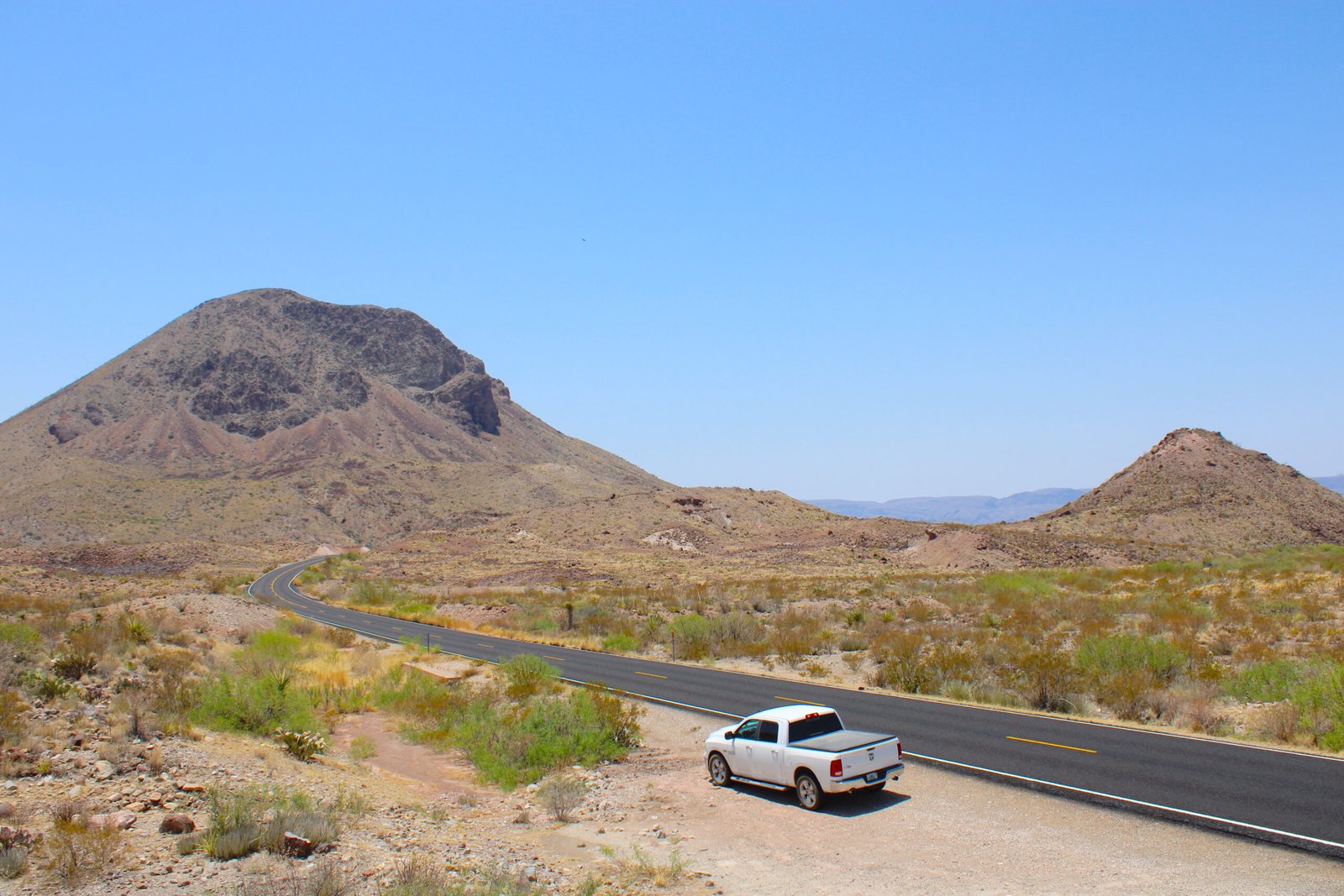 hite pickup truck navigating a winding curve along a scenic desert canyon road in West Texas.