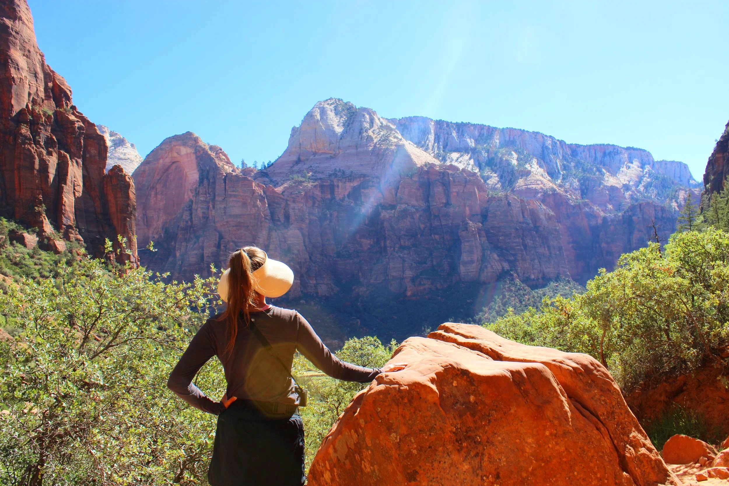 Hiker enjoying the panoramic view of the Watchman and surrounding red rock formations from the overlook on the Watchman Trail in Zion National Park
