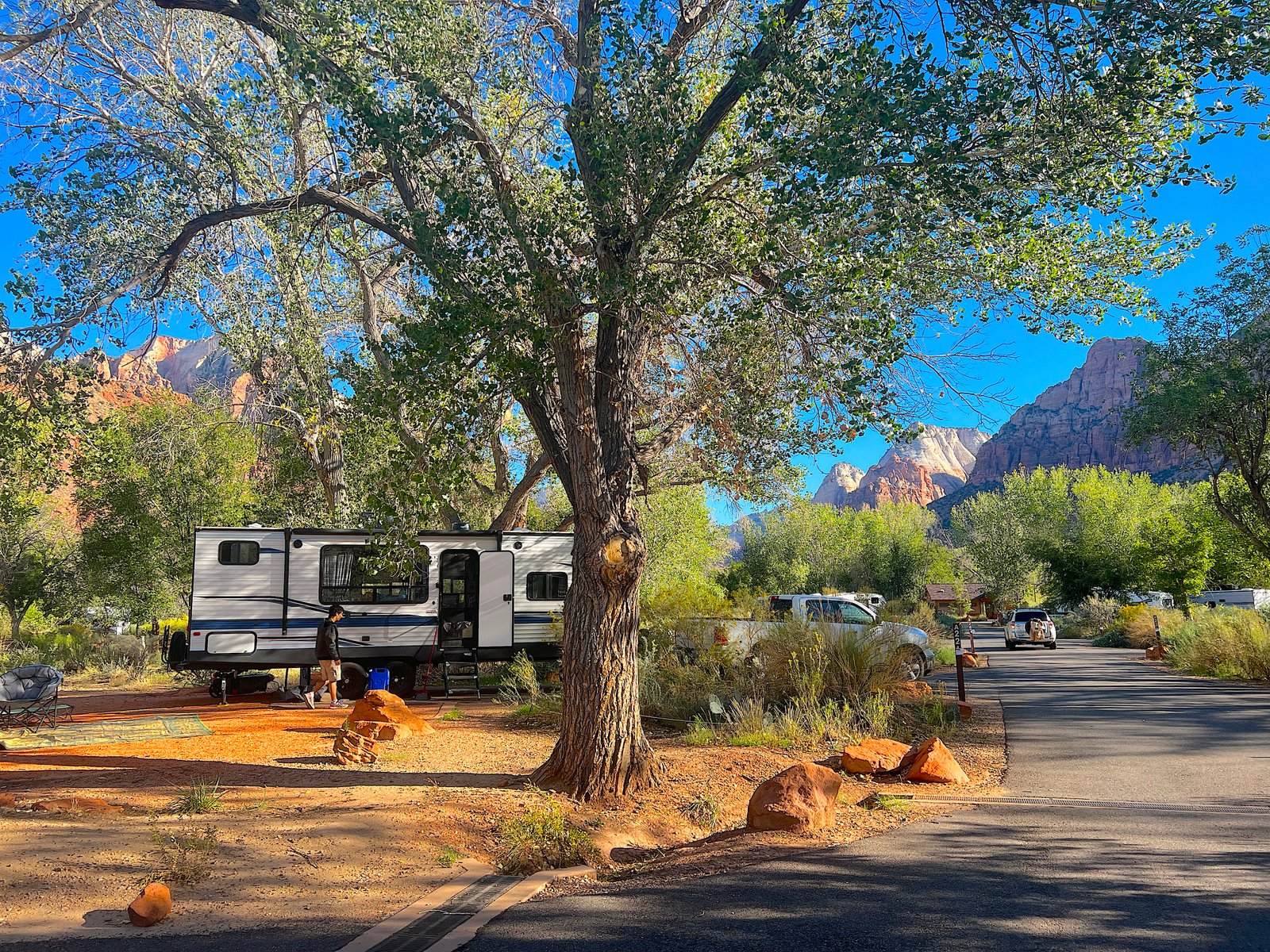 An RV parked at a scenic campsite surrounded by scrub oak and towering red rock cliffs at Watchman Campground in Zion National Park.