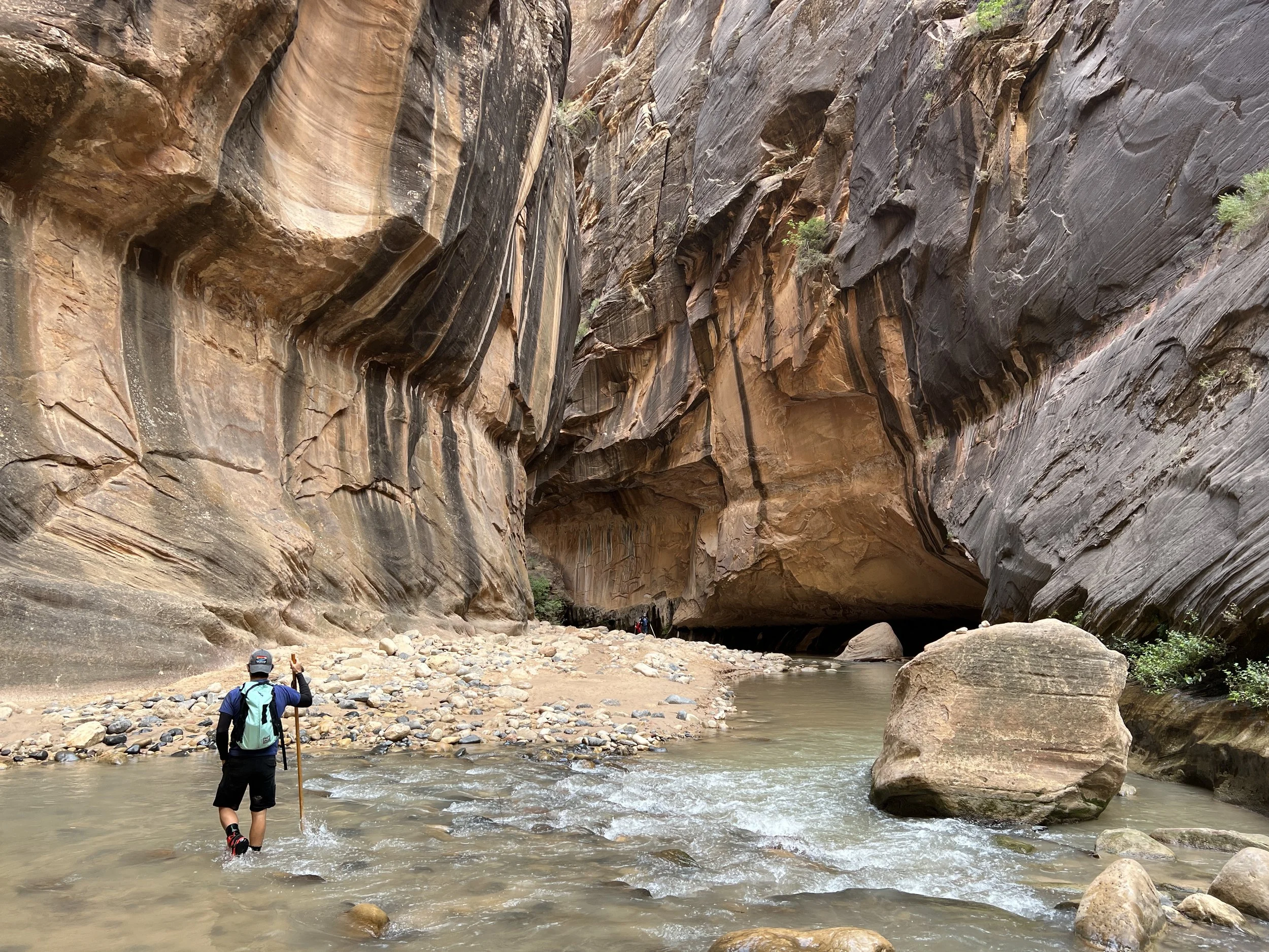 Hiker wading through the deep water of The Narrows in Zion National Park using a walking stick and rental gear