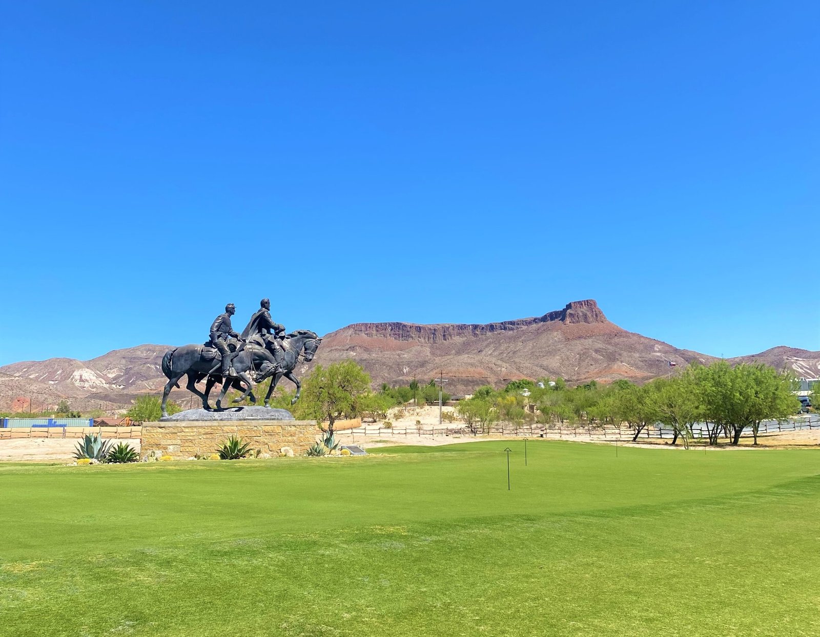 Green golf course fairway and equestrian bronze statue set against rugged desert mountains at Lajitas Golf Resort.