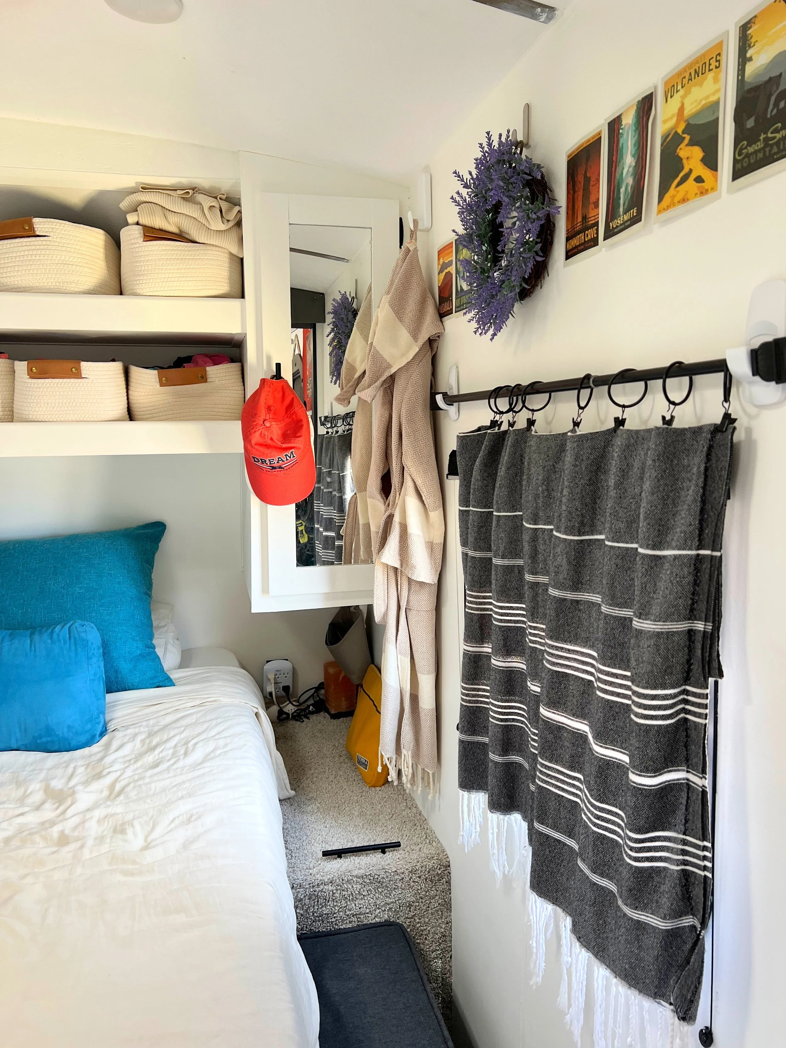 A wider view of an RV bedroom showcasing a no-sew Turkish towel curtain hung over the window with Command hooks and a black rod