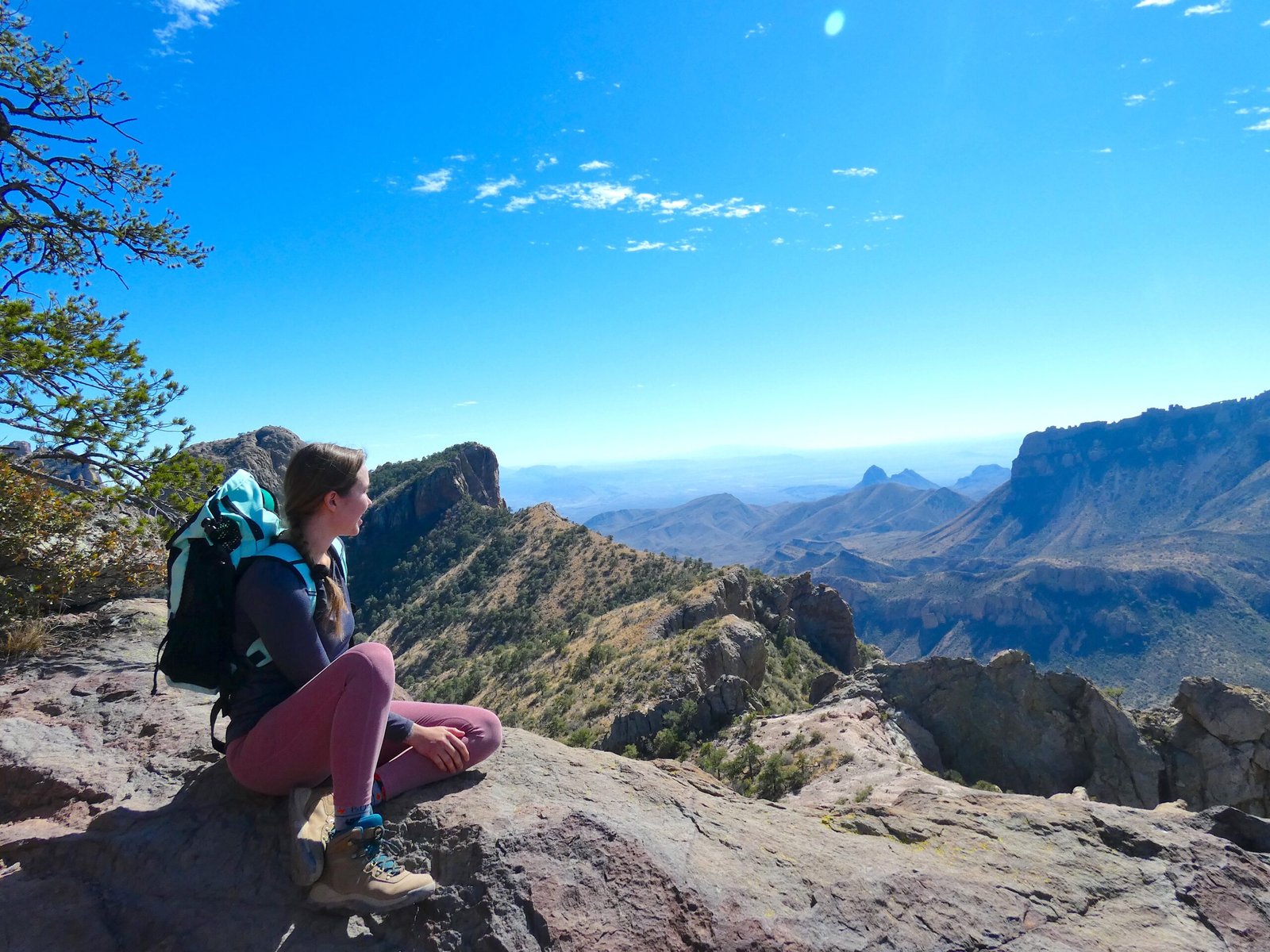 Female hiker sitting on a rocky cliff overlook admiring the Chisos Mountains along the Lost Mine Trail in Big Bend National Park.
