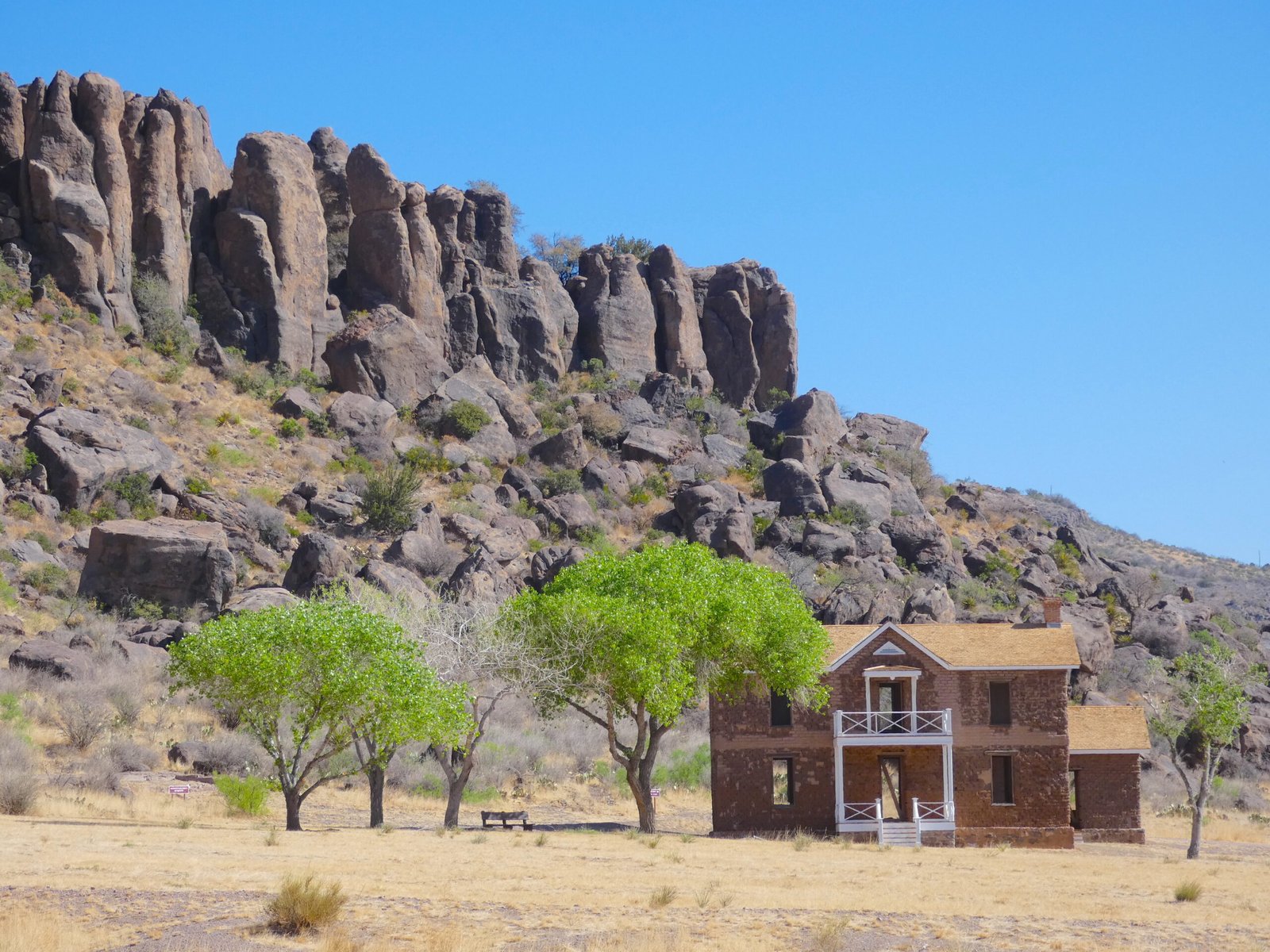 Two-story historic stone building surrounded by trees and dramatic rocky cliffs at Fort Davis National Historic Site in West Texas.