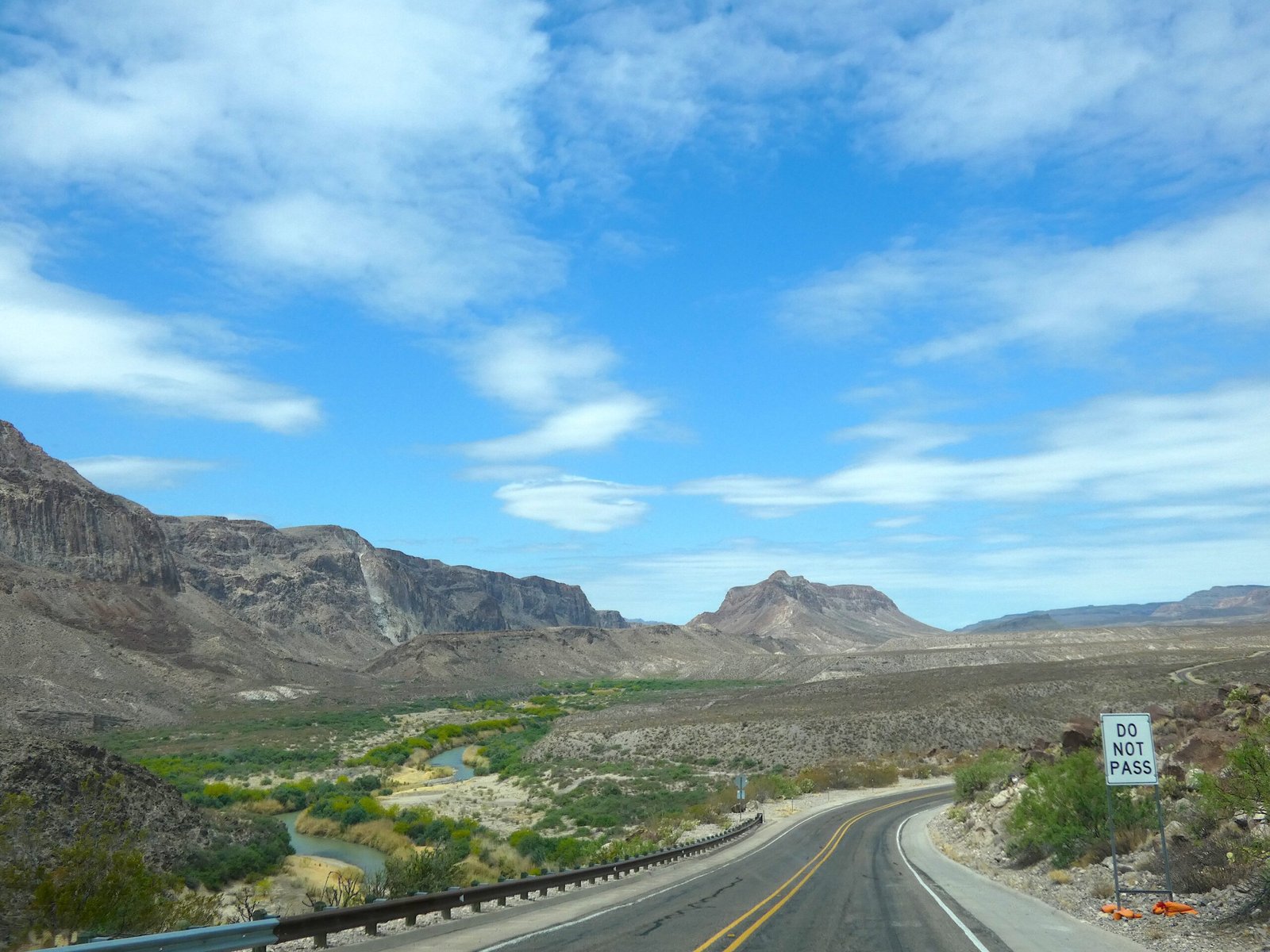 Asphalt road of FM 170 winding next to the Rio Grande river with desert hills and blue sky in Big Bend Ranch State Park.