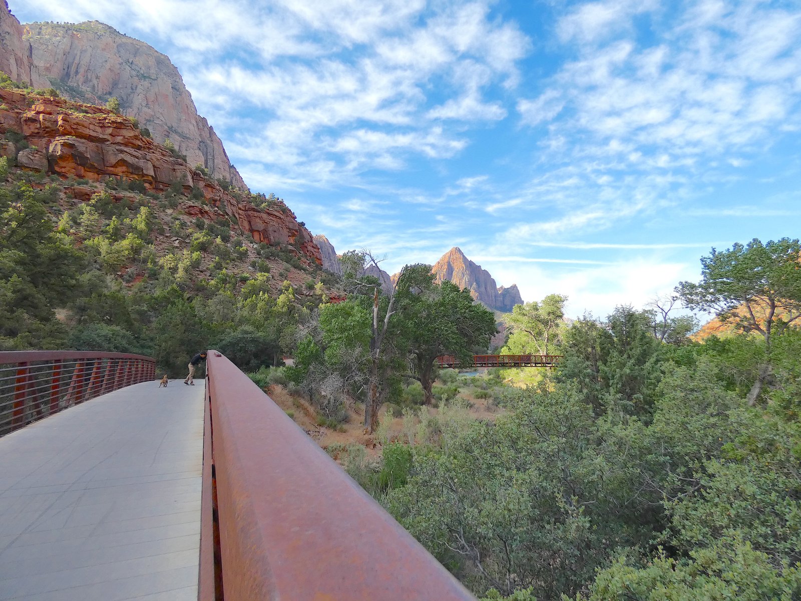 View of the paved Pa'rus Trail running alongside the Virgin River and the red metal footbridge in Zion National Park
